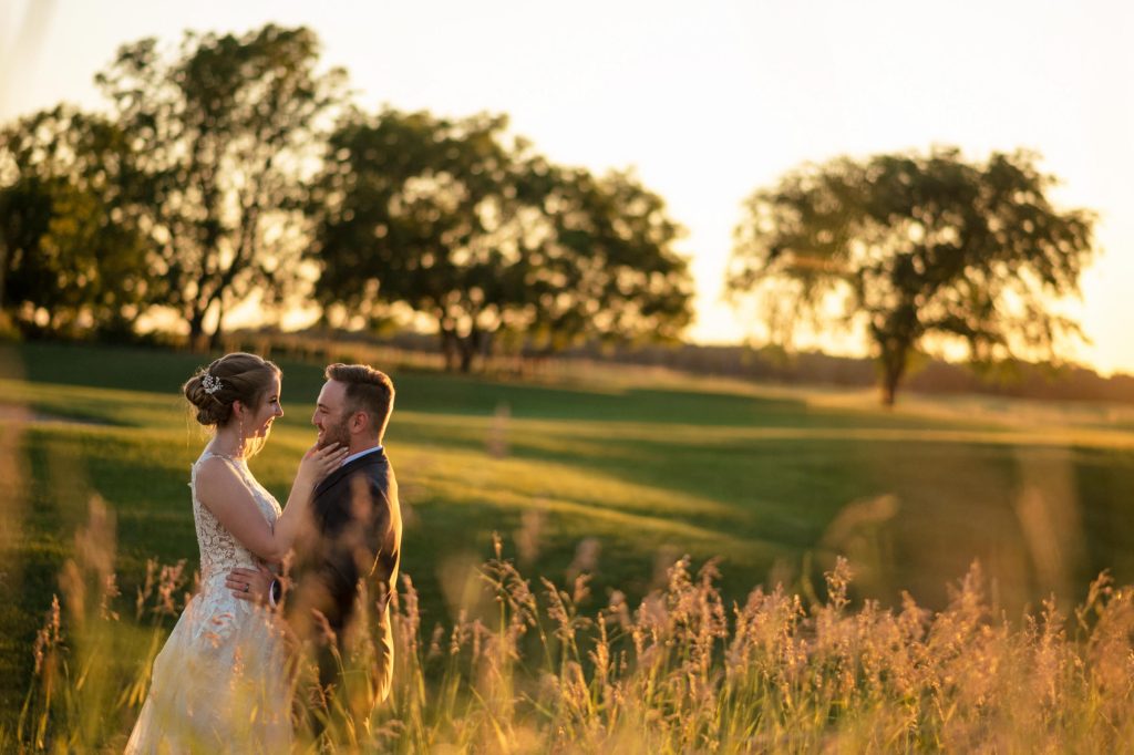 Bride and groom, embracing and looking into each other's eyes with nature, and a beautiful sunset in the background