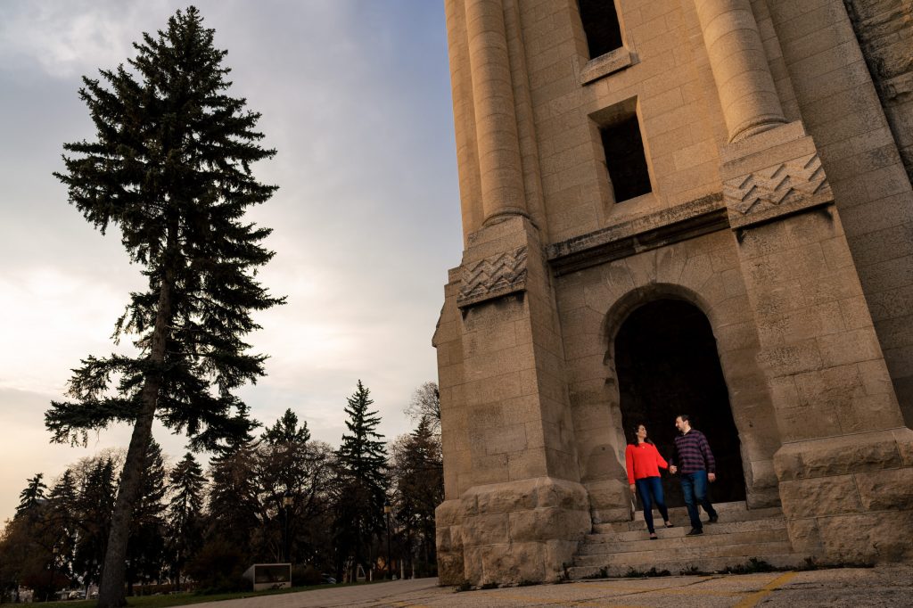 And engage walking and holding hands out of stone door with trees around at Saint Boniface Cathedral in Winnipeg