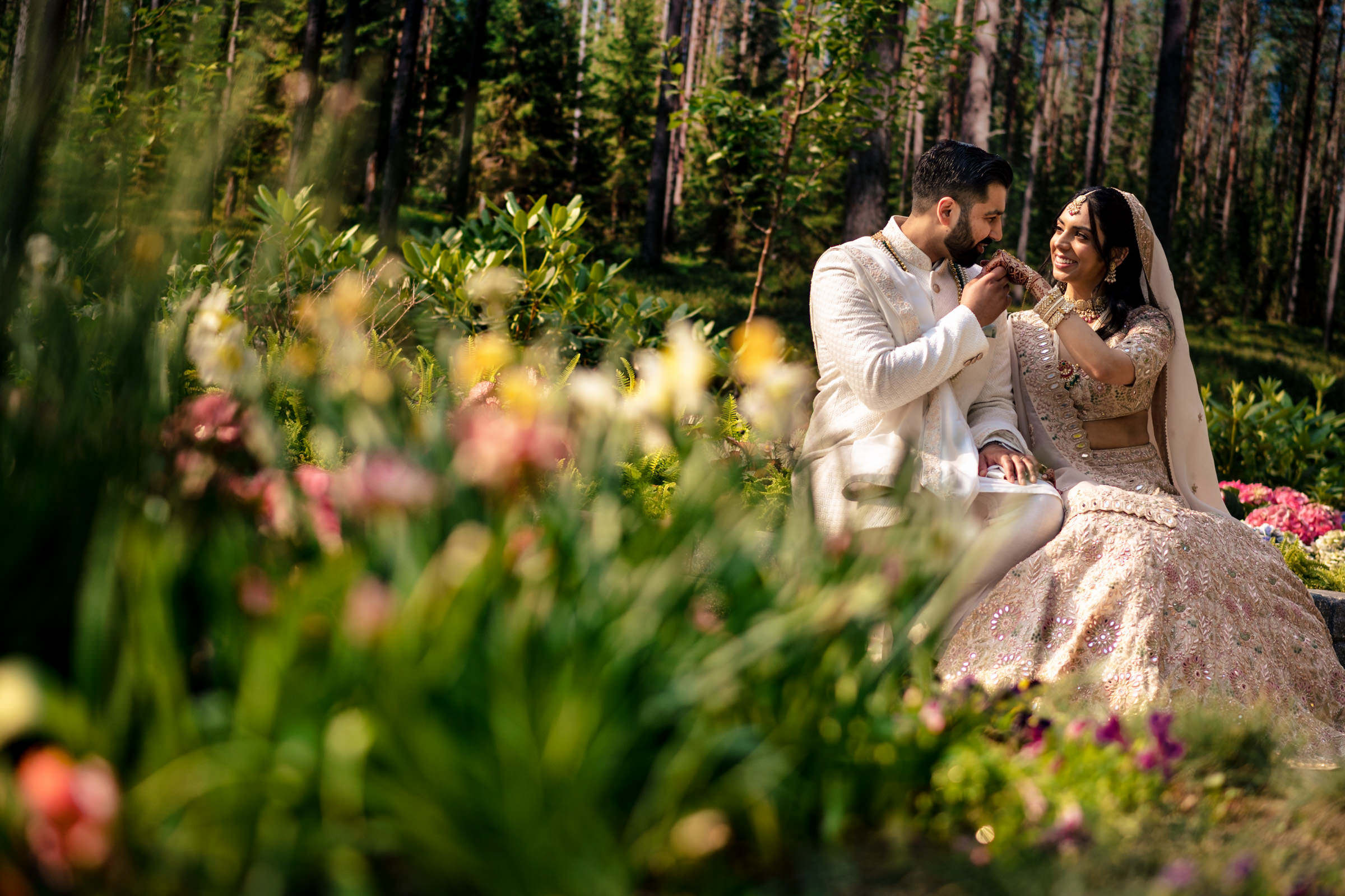 A couple in wedding attire sits joyfully in a lush Winnipeg wedding venue full of colorful flowers.