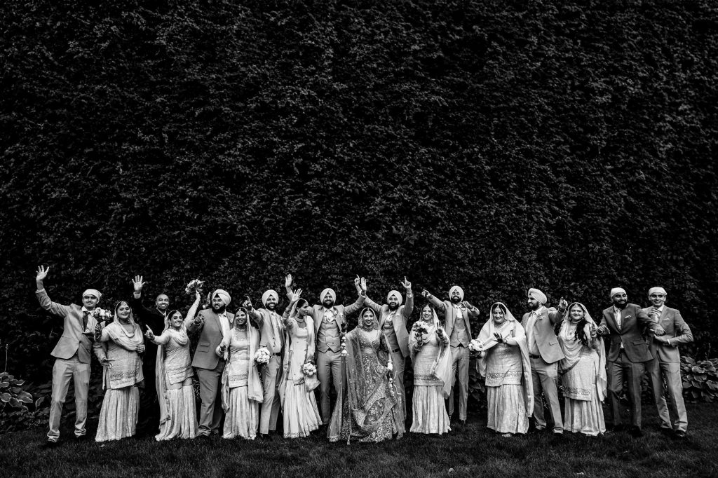 Bride and groom, with their huge wedding party, dancing in front of a vine wall in black-and-white