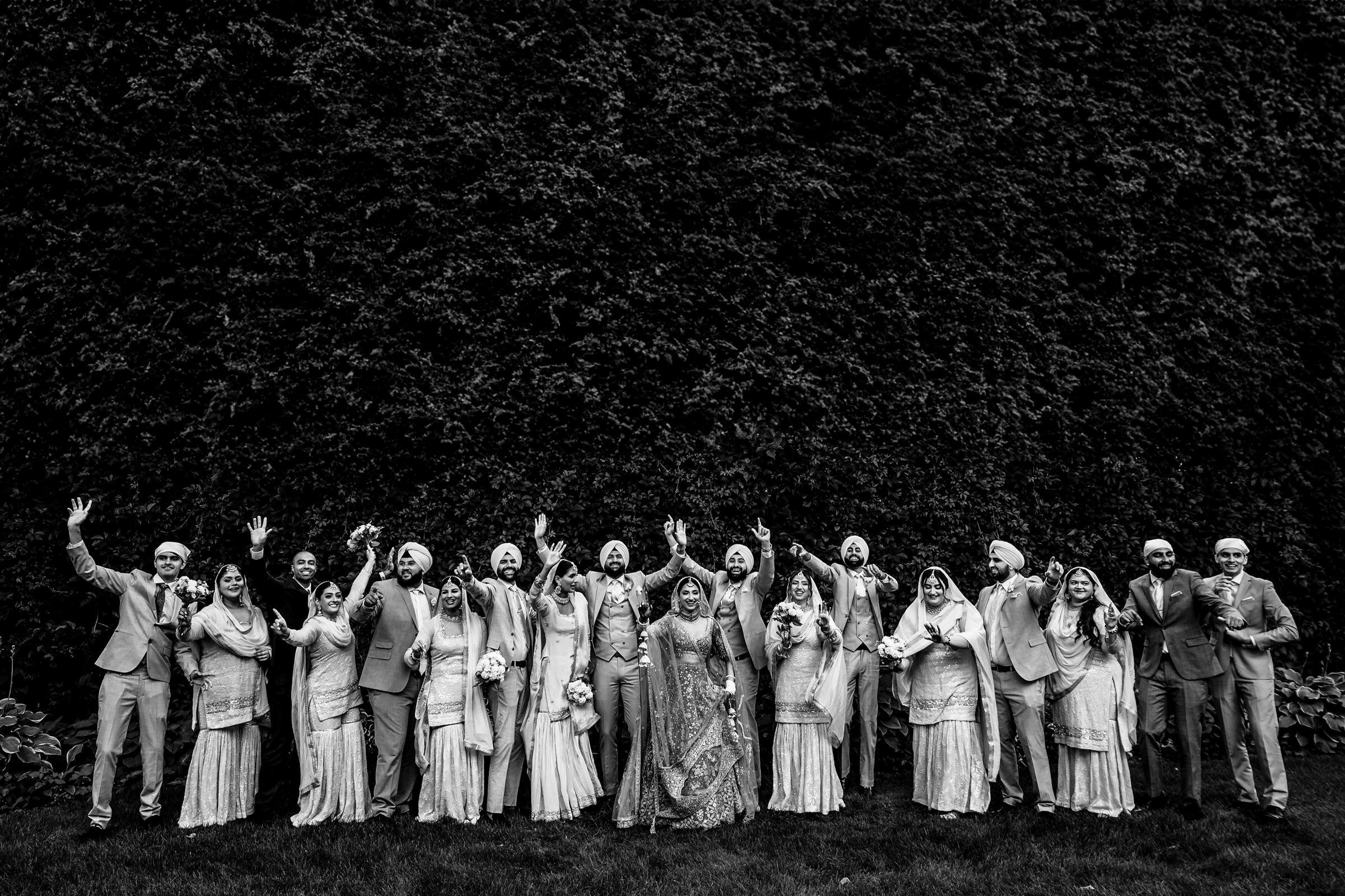 A wedding photographer captures a joyful party in traditional attire against a lush backdrop.