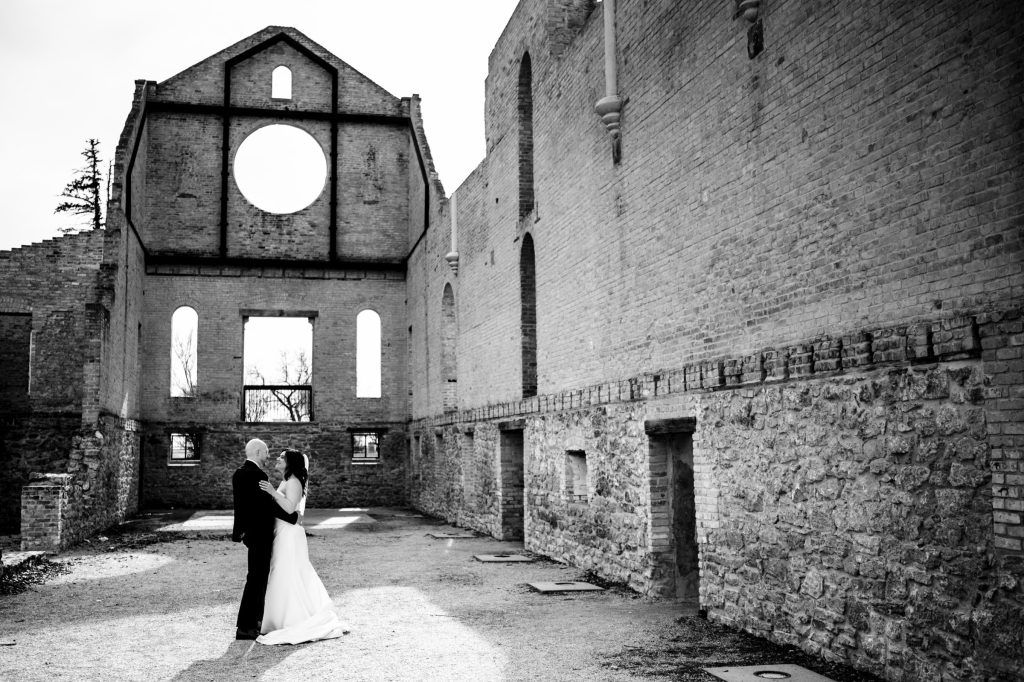 Bride and groom, dancing for a wedding photo, surrounded by a stone wall at the Trappest monastery in Winnipeg Manitoba