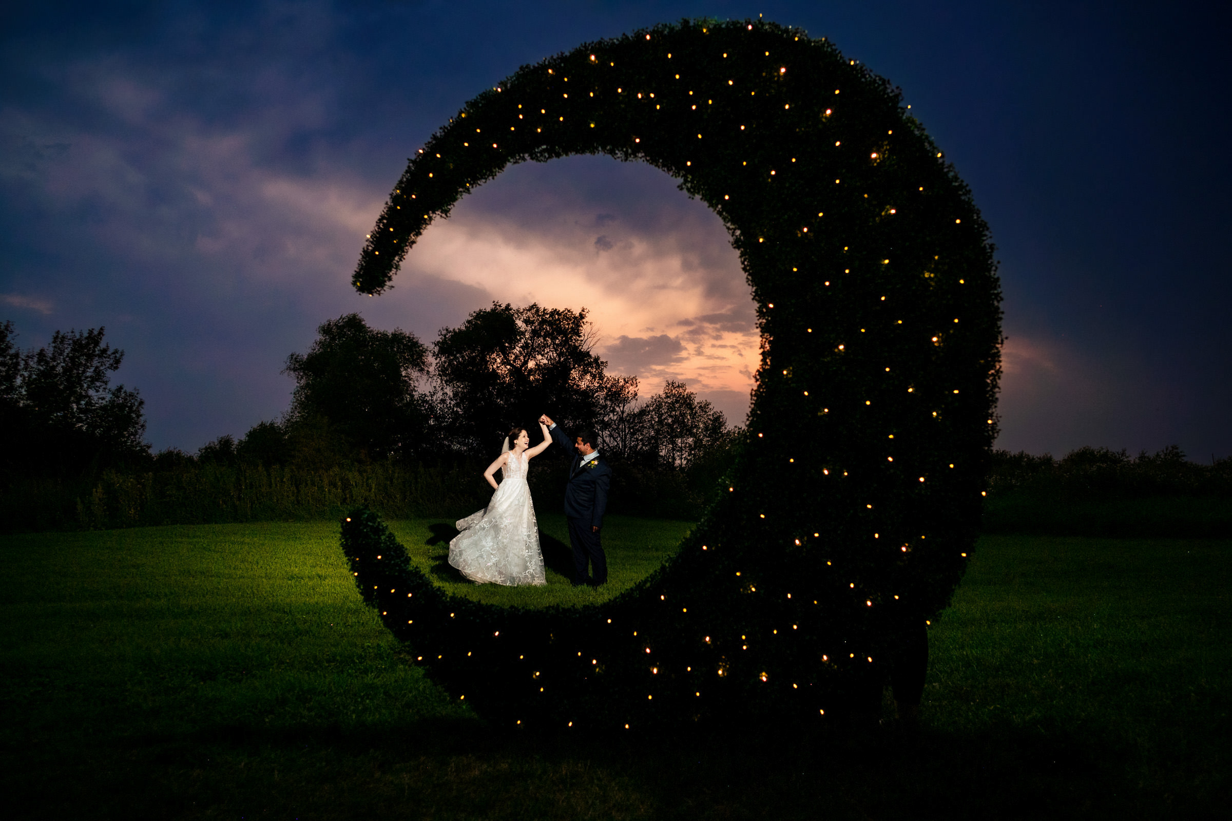 bride and groom dancing in a field at night at a wedding through a moon.
