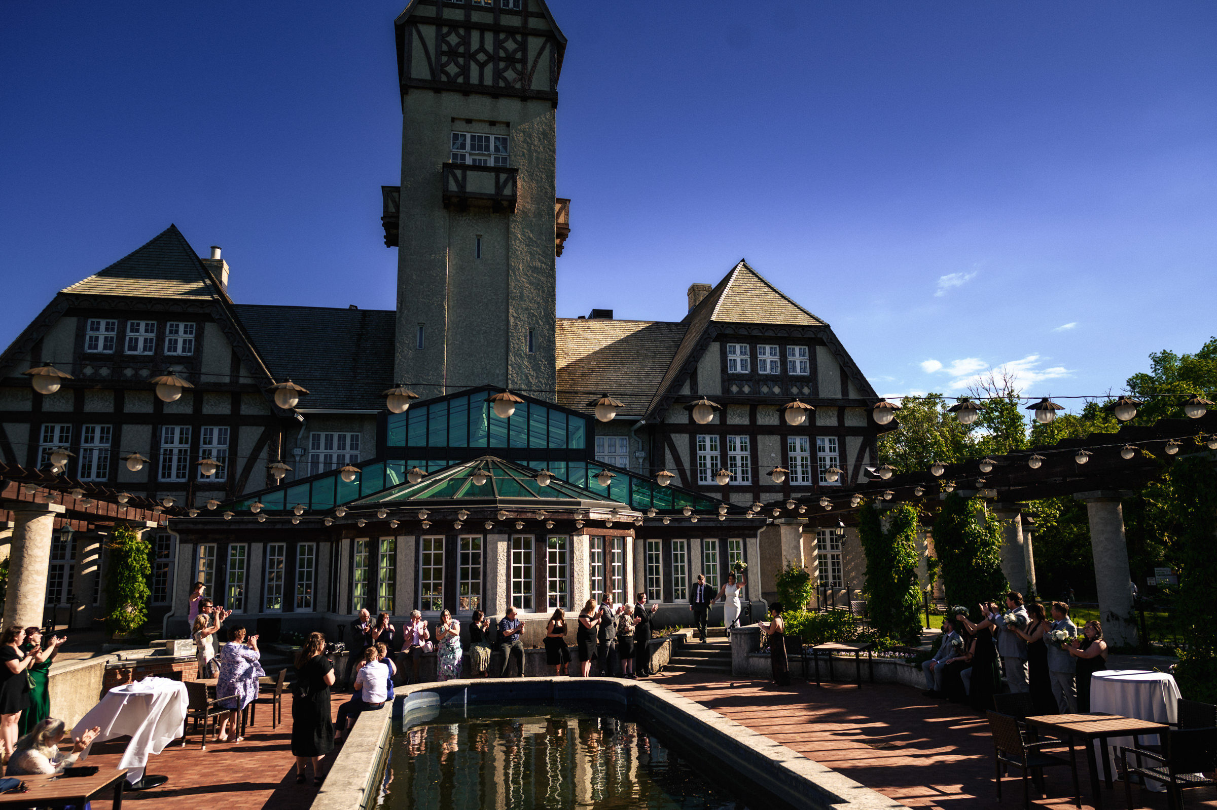 People gather at a historic Winnipeg wedding venue with a tower and reflective pool.