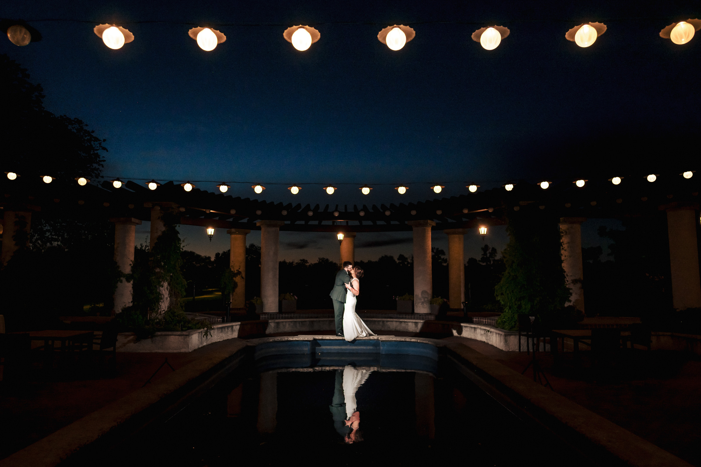 Newlywed couple dancing by a pool under Winnipeg wedding venue lights at night.