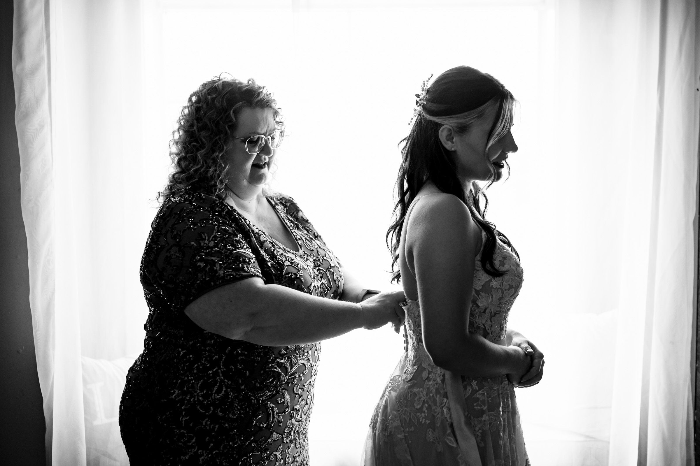 Woman assists bride with dress at a softly lit Winnipeg wedding venue.