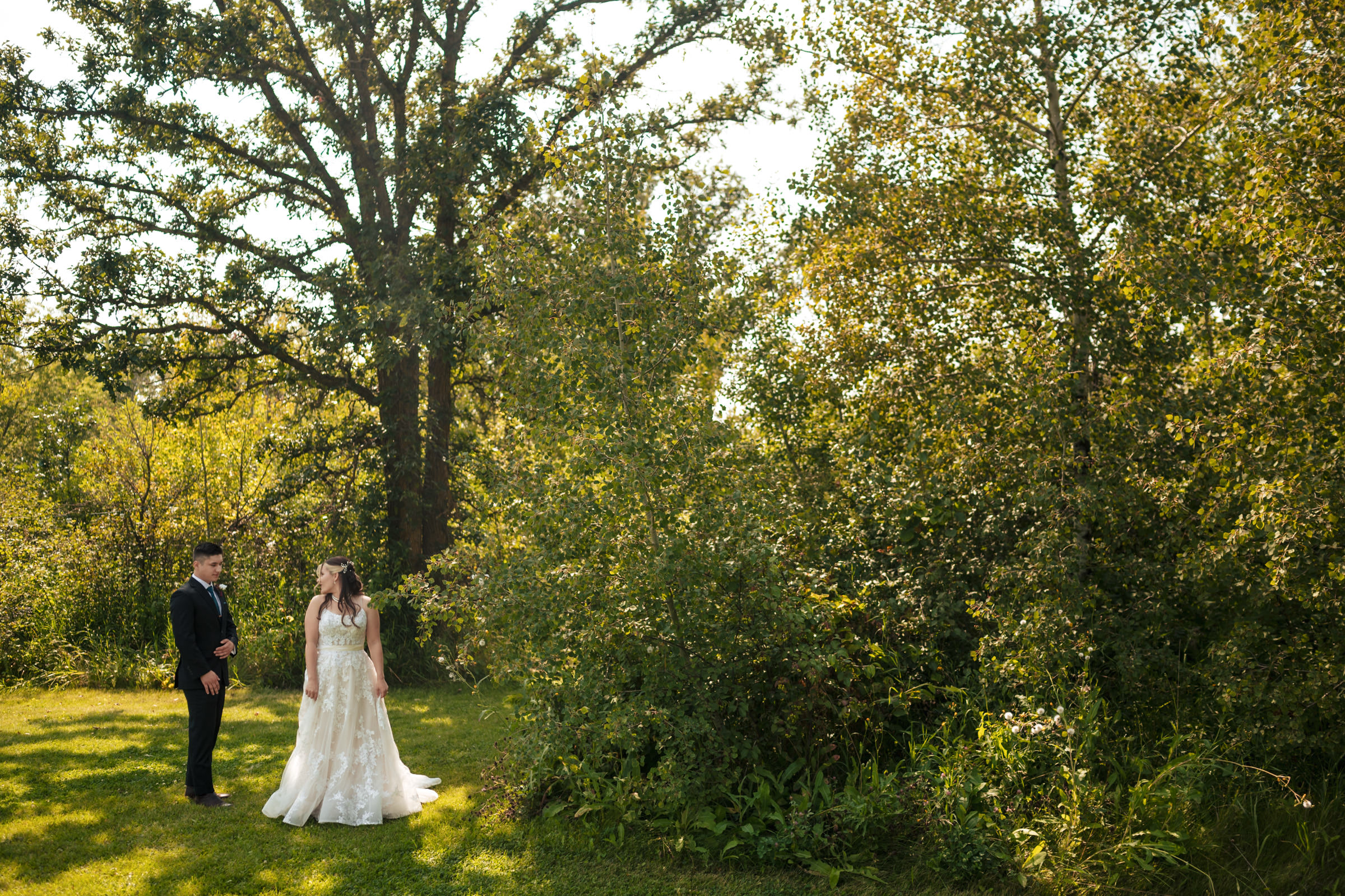Bride and groom stand together outdoors, surrounded by lush greenery at a Winnipeg wedding venue.