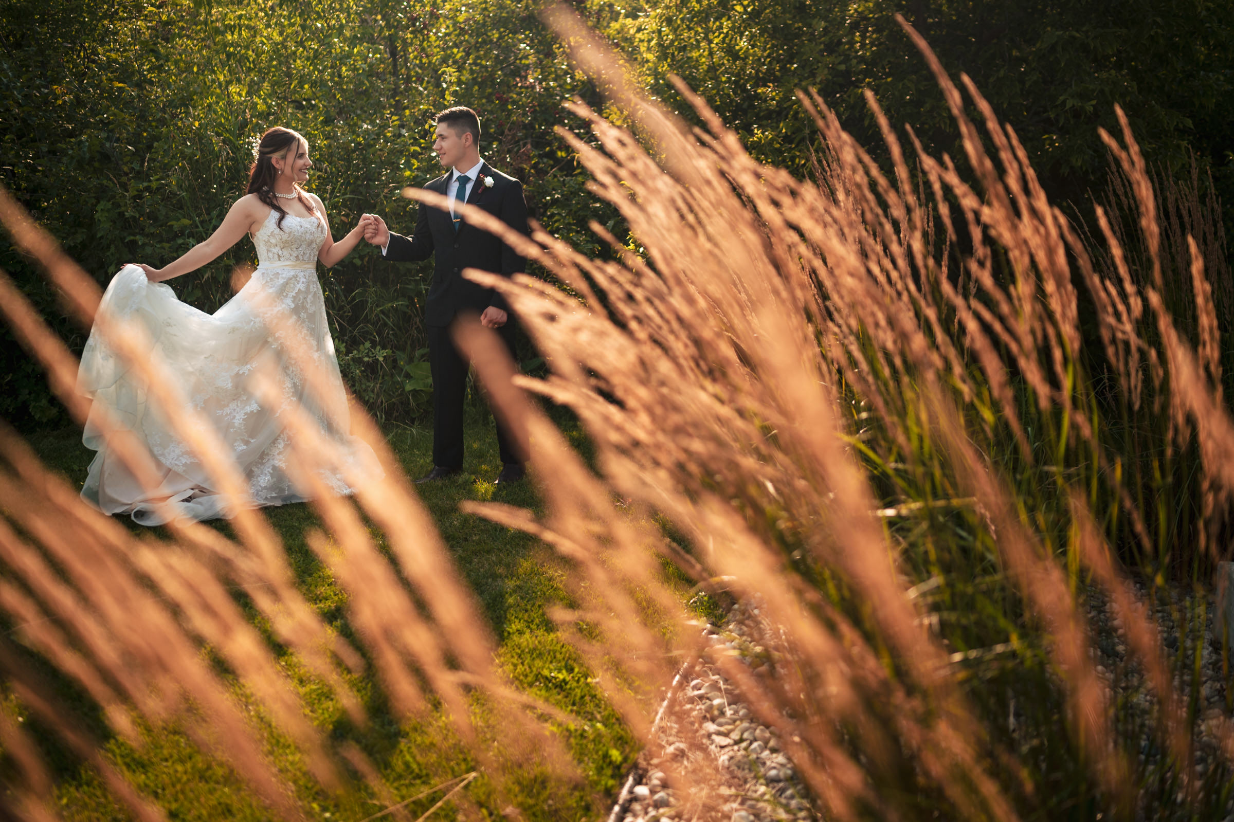 Bride and groom holding hands, smiling, in a sunlit garden at Winnipeg wedding venues.