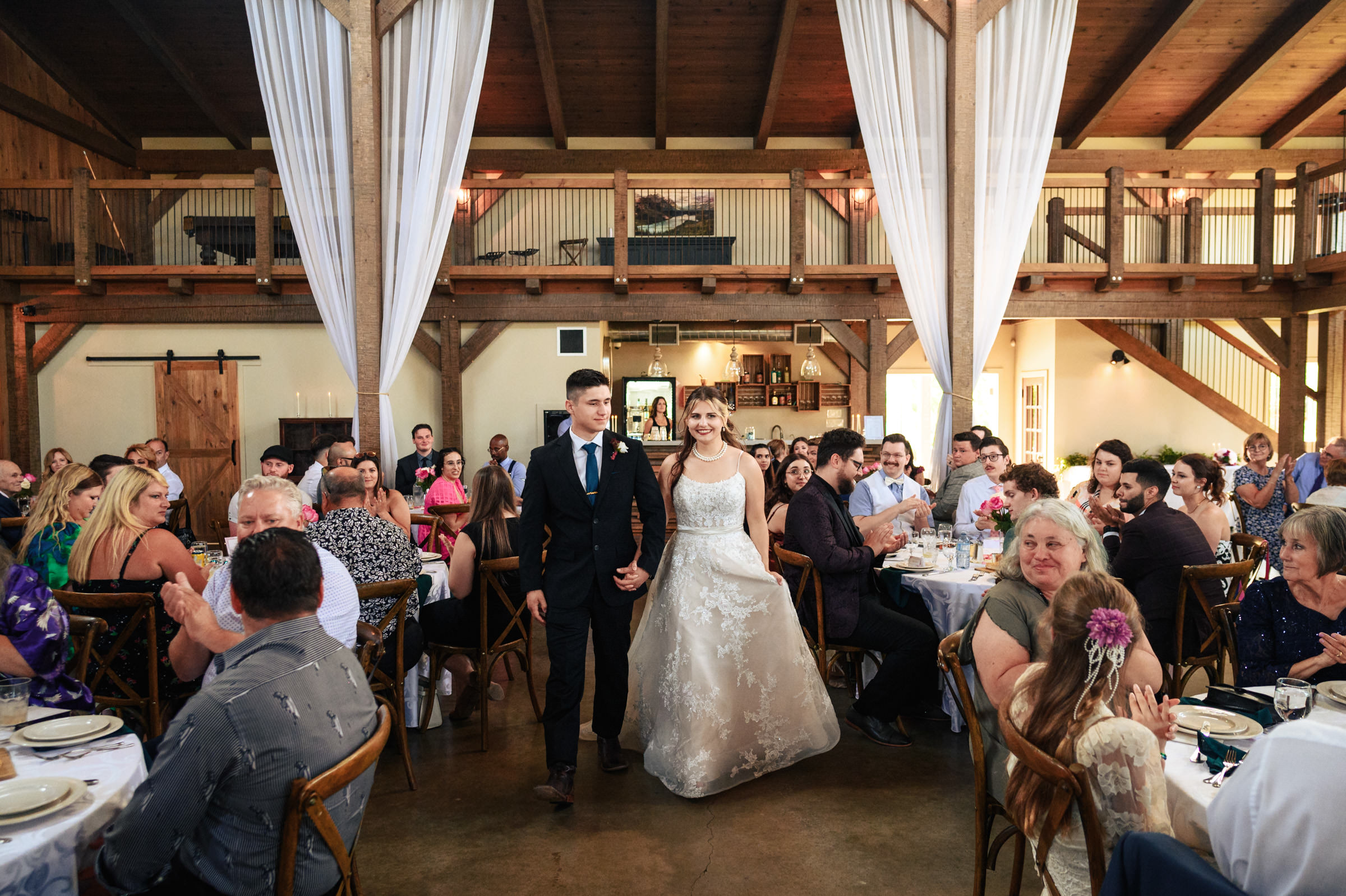 Bride and groom enter a rustic Winnipeg wedding venue, guests seated at decorated tables.