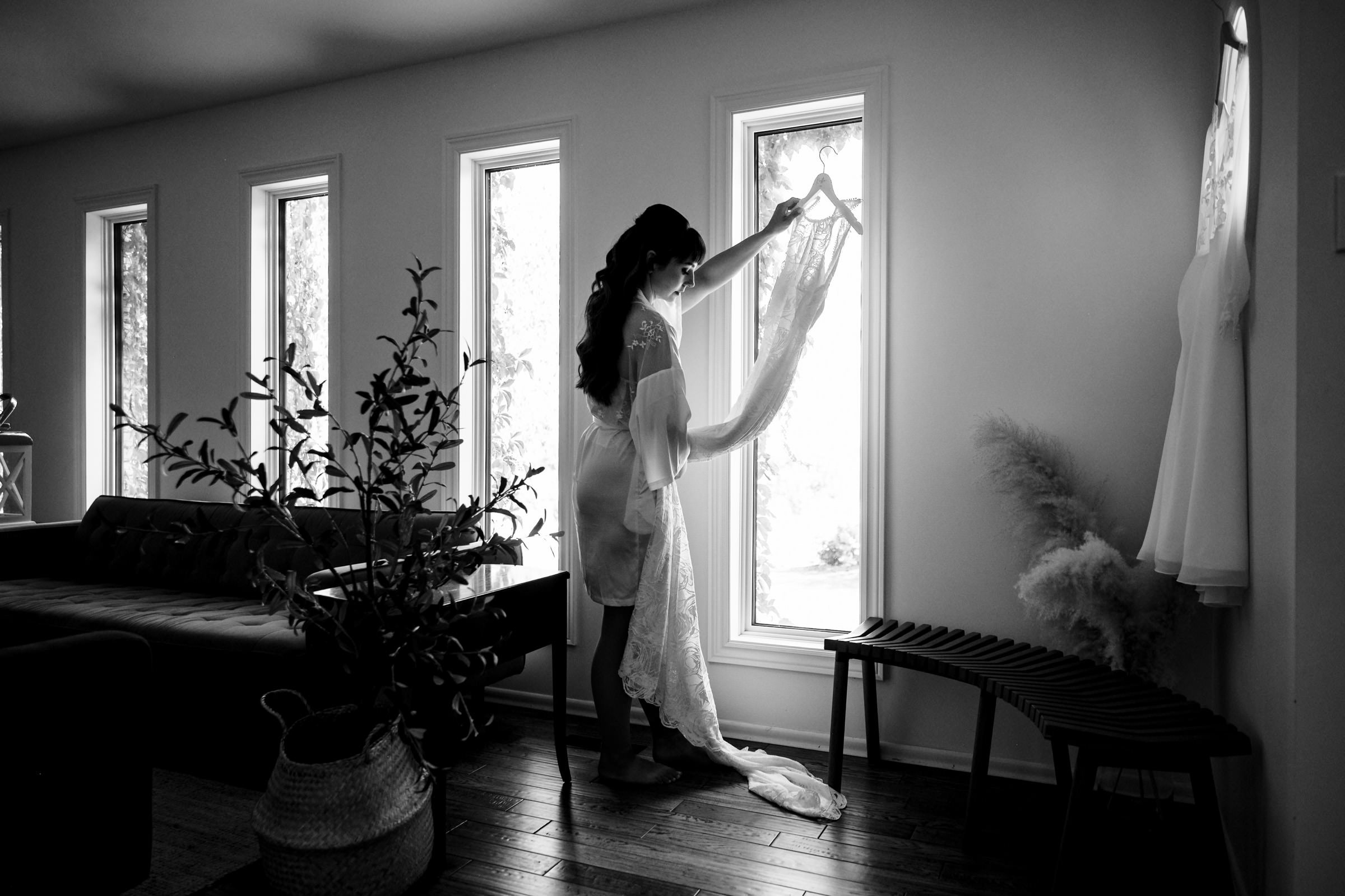 Bride holding a dress by a window in Winnipeg's softly lit wedding venue.
