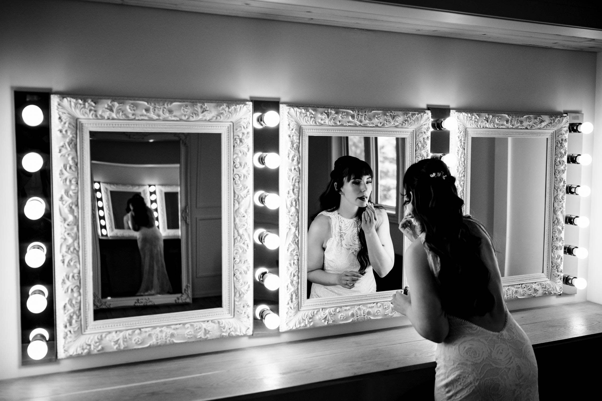 Bride adding lipstick in front of three mirrors at a top Winnipeg wedding venue.