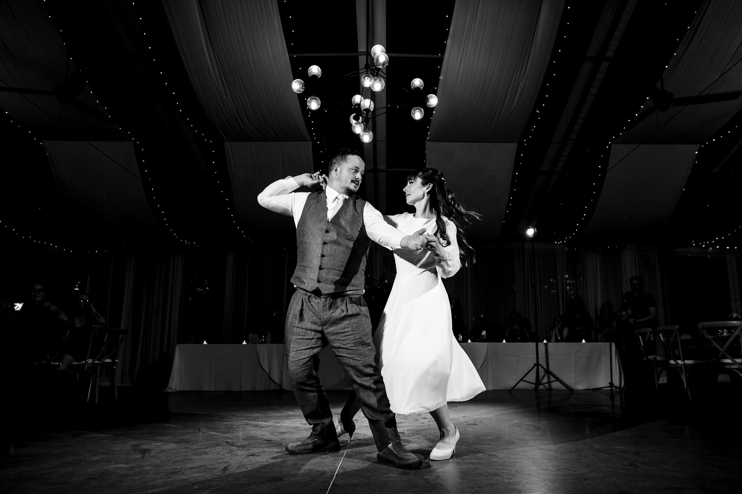 A couple dances joyfully under twinkling lights at a Winnipeg wedding venue.
