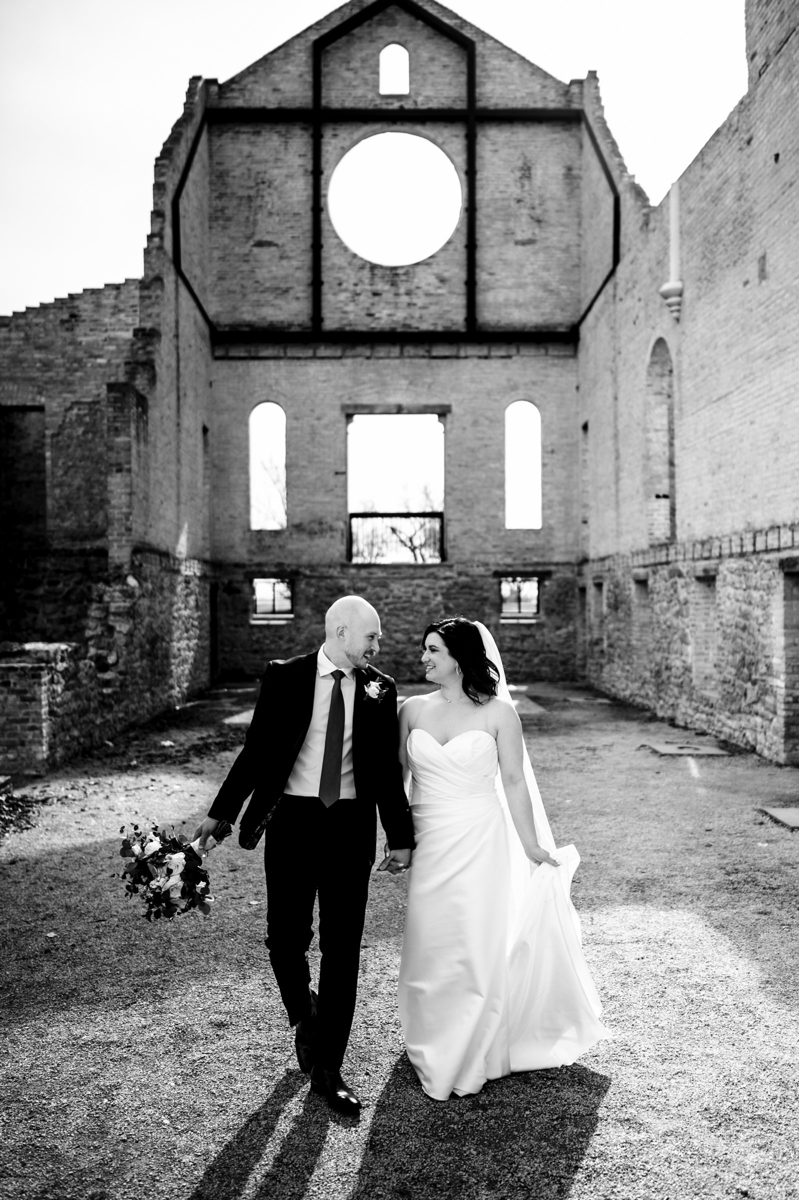 Bride and groom walk hand-in-hand through the stunning stone ruins, showcasing their love during their intimate wedding in Winnipeg.