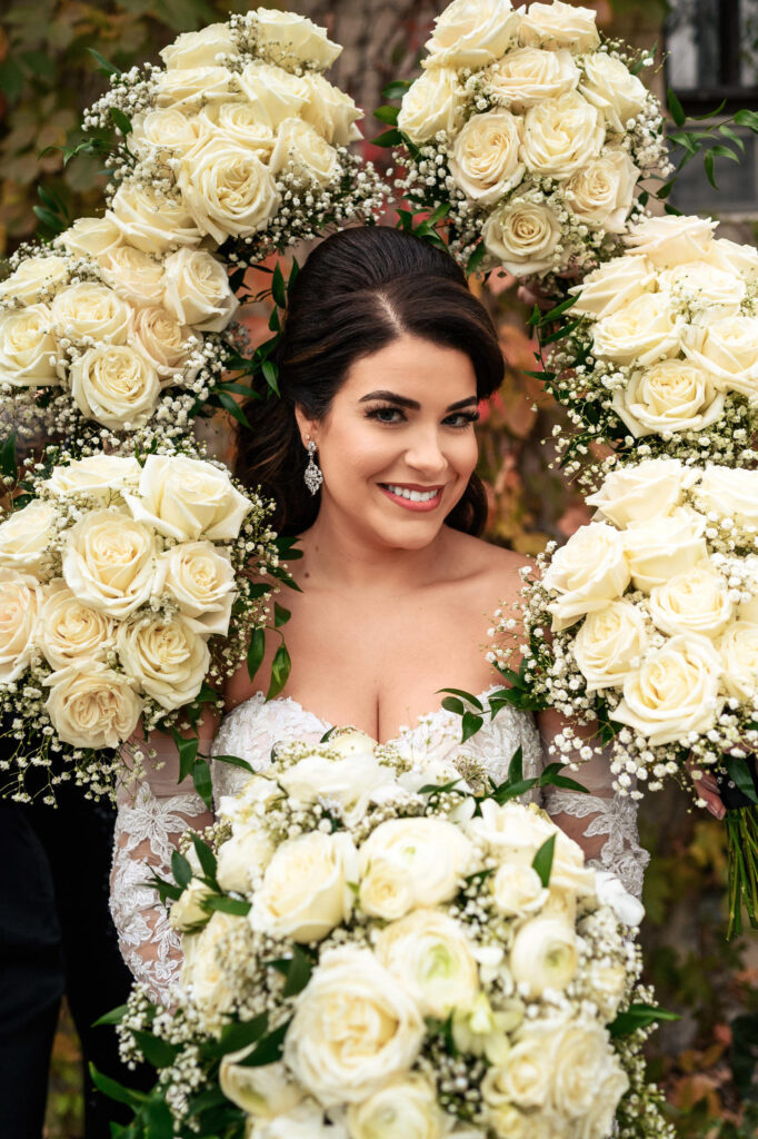 Bride at fall wedding in Winnipeg, surrounded by cream rose bouquets, smiling warmly.