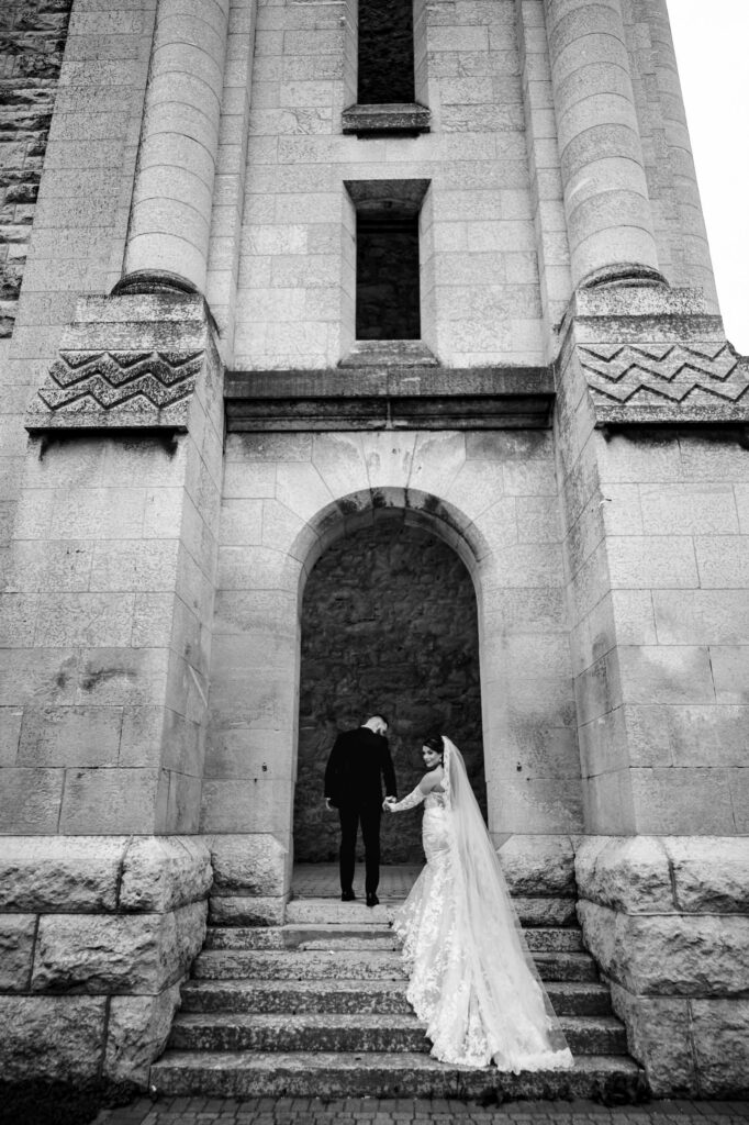 Bride and groom on stone steps at a tall arch, capturing a fall wedding in Winnipeg.