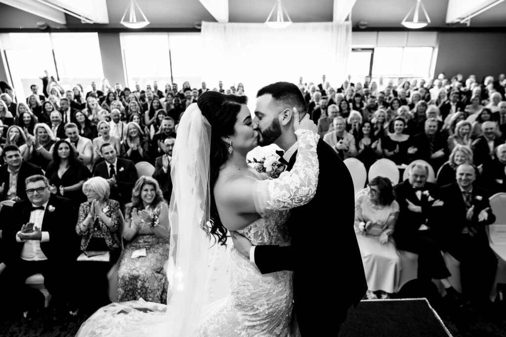 Bride and groom kissing at their fall wedding in Winnipeg, with guests watching.