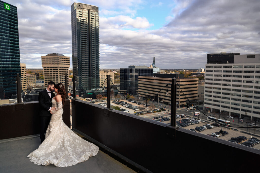 Bride and groom embrace on a rooftop during their fall wedding overlooking Winnipeg's cityscape.