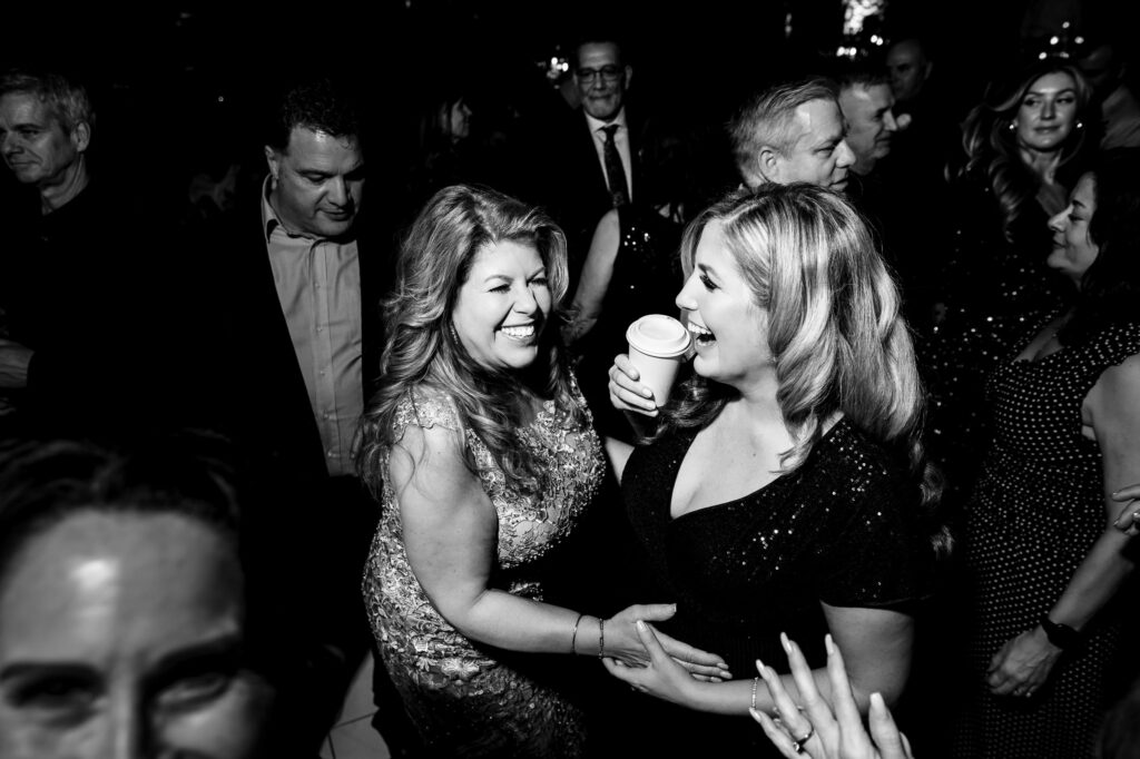 Two women at a fall wedding in Winnipeg, smiling and holding a coffee cup.
