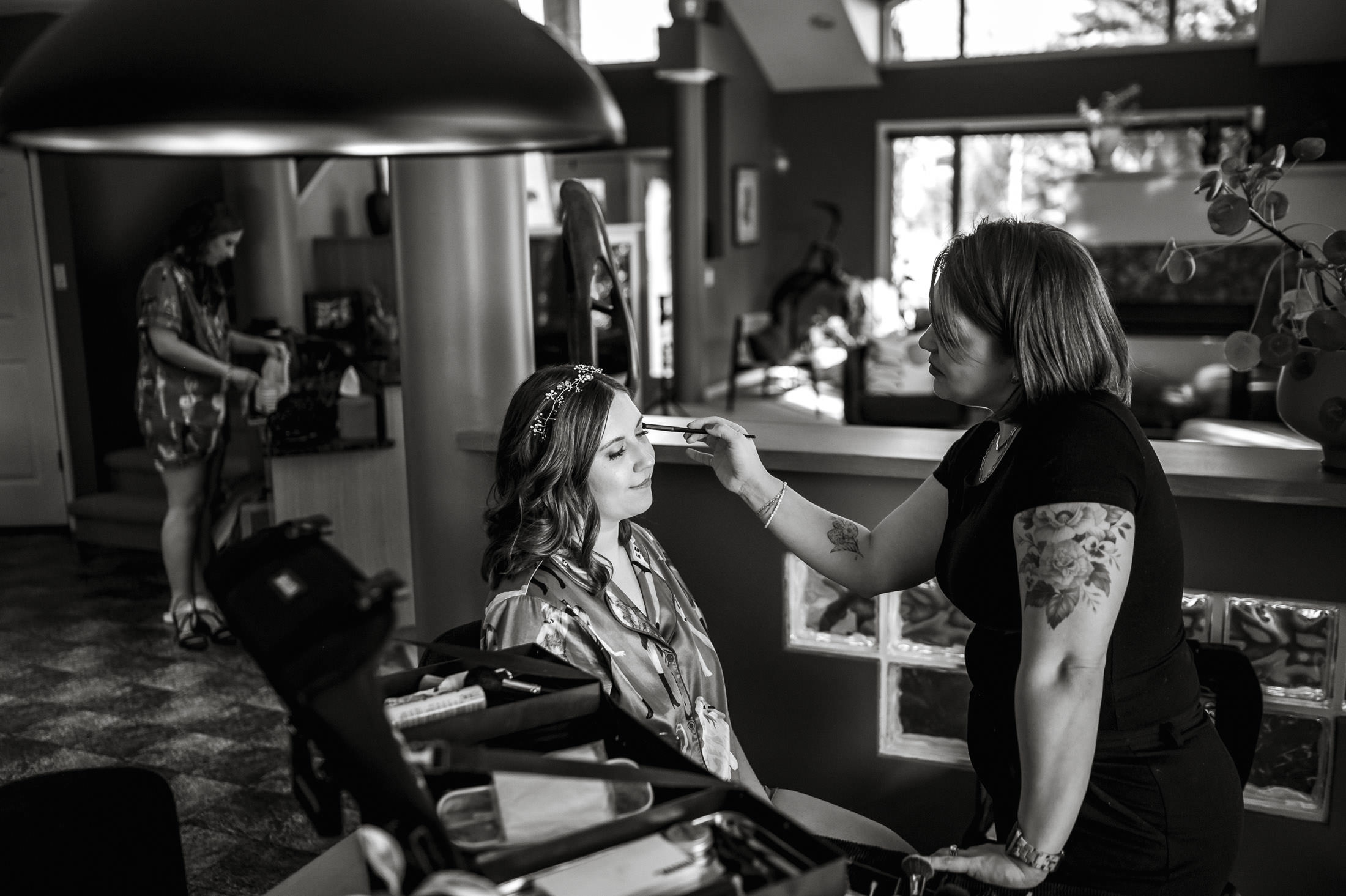 Makeup artist preps a woman for winter wedding photos at The Leaf, in a well-lit room.