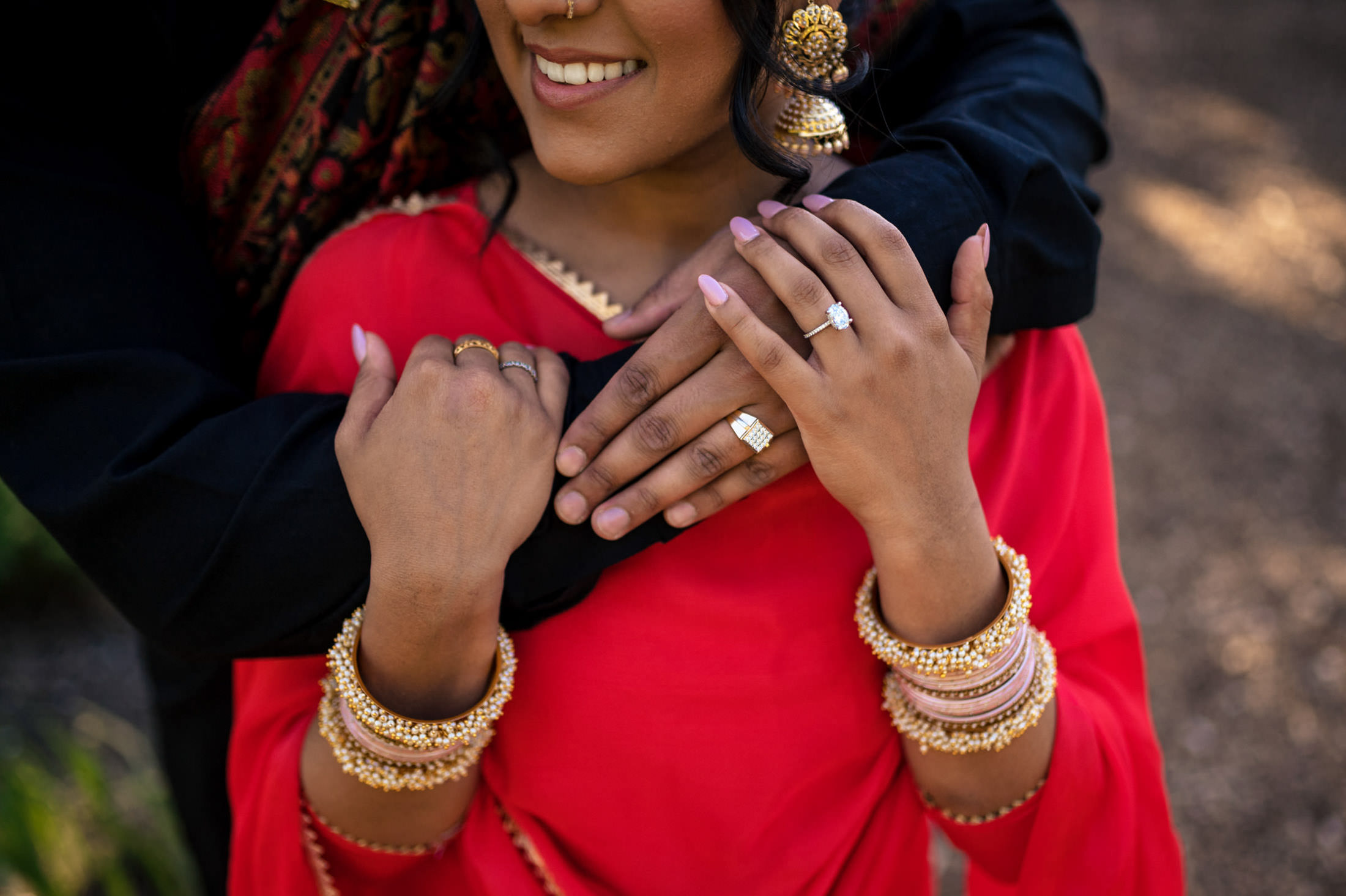 Couple embracing, showcasing jewelry and rings, with the woman wearing a red outfit.