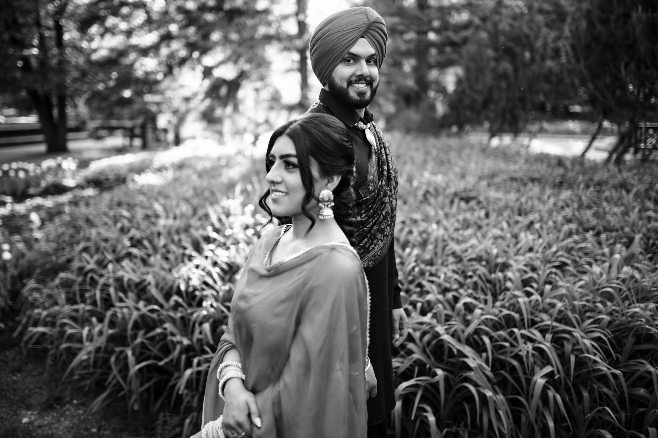 Couple in traditional attire standing in a lush garden, smiling.