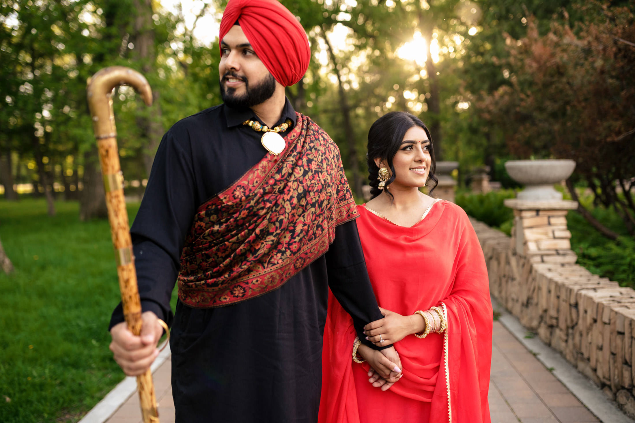 Couple in traditional attire walking hand in hand in a park.