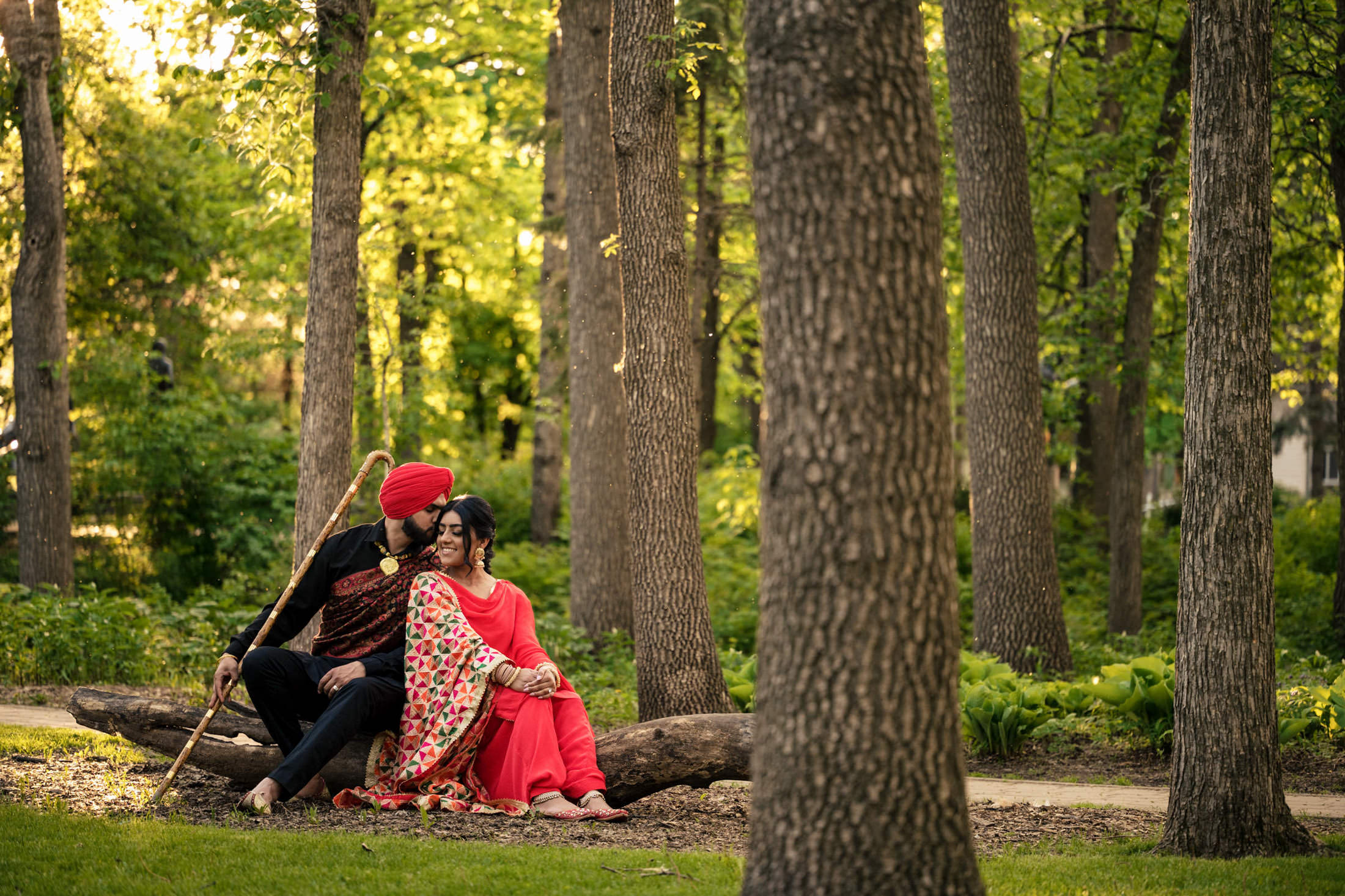 Couple in traditional attire sitting in a forest, gazing at each other lovingly.