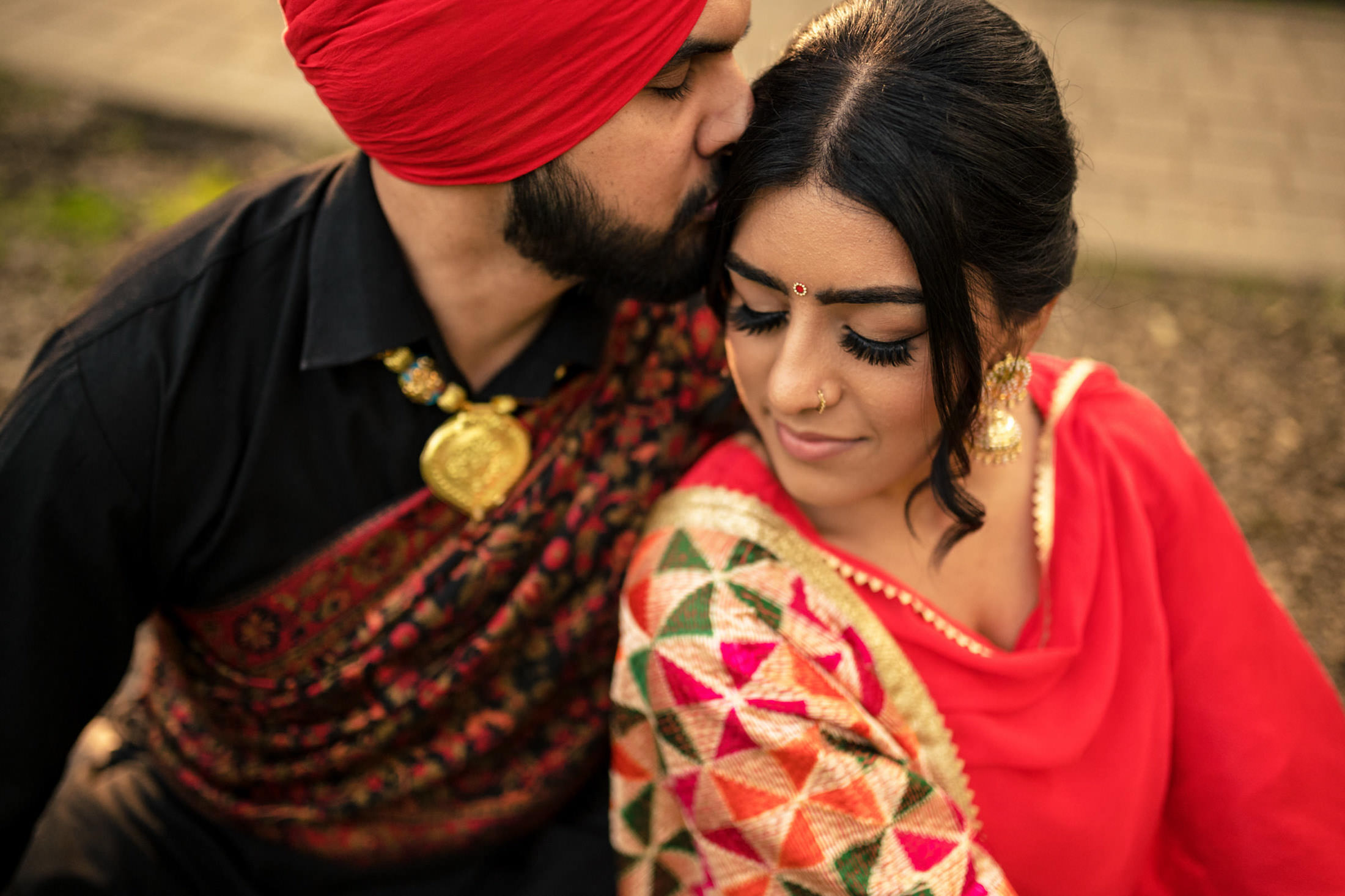 A couple in colorful traditional attire, man kissing woman's head.