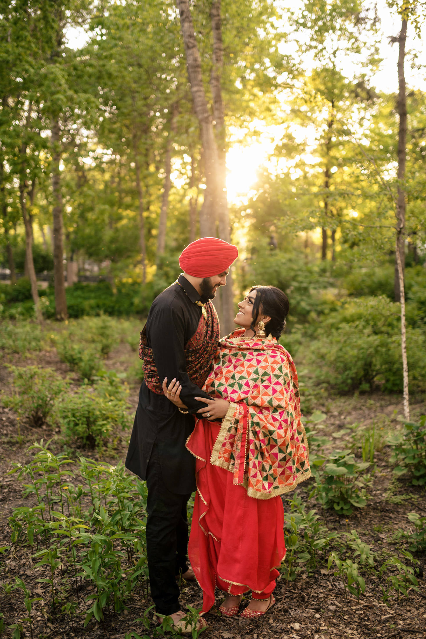 A couple in colorful attire embraces in a sunlit forest.