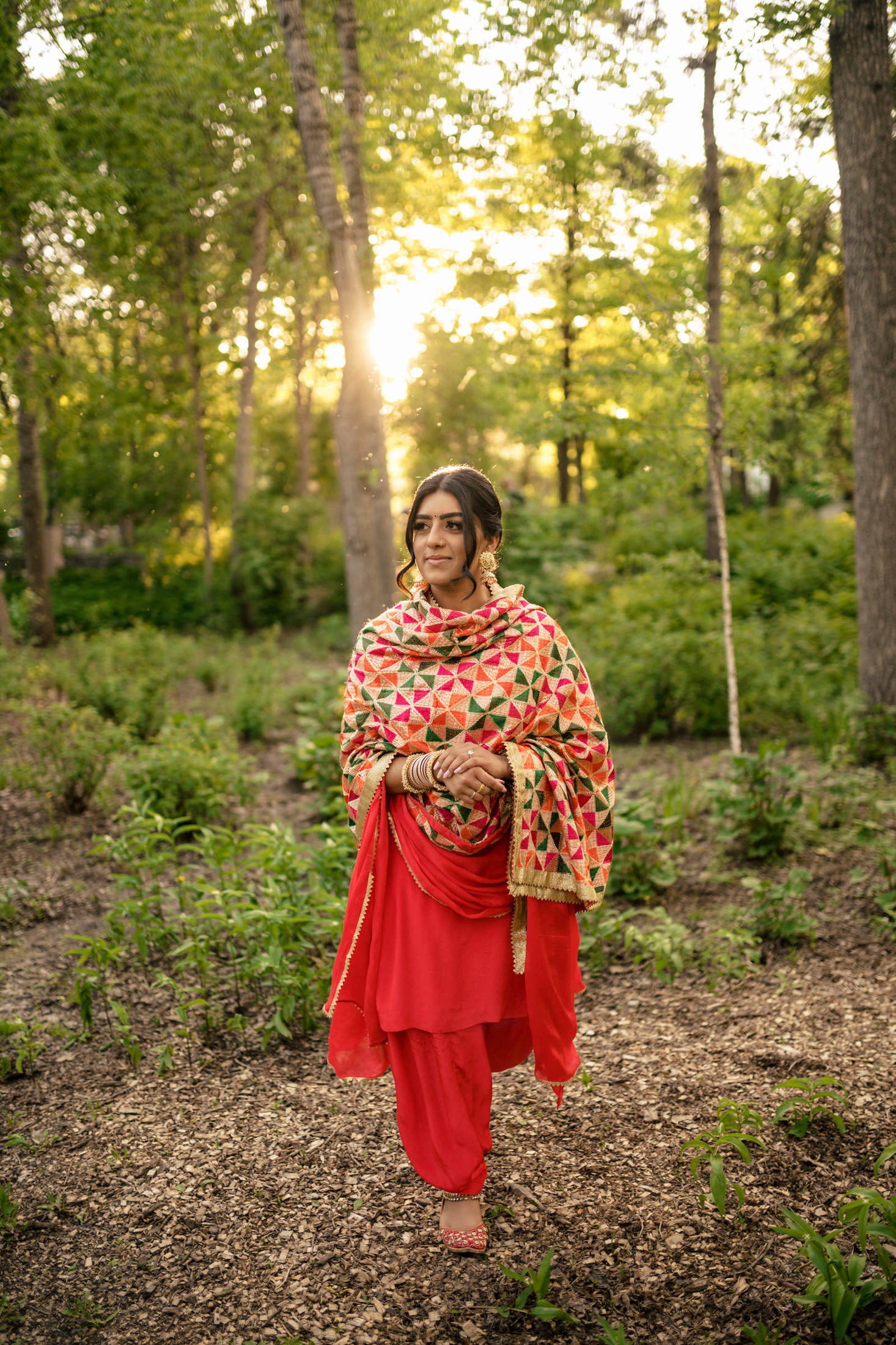 Woman in red traditional attire walking in a sunlit forest.
