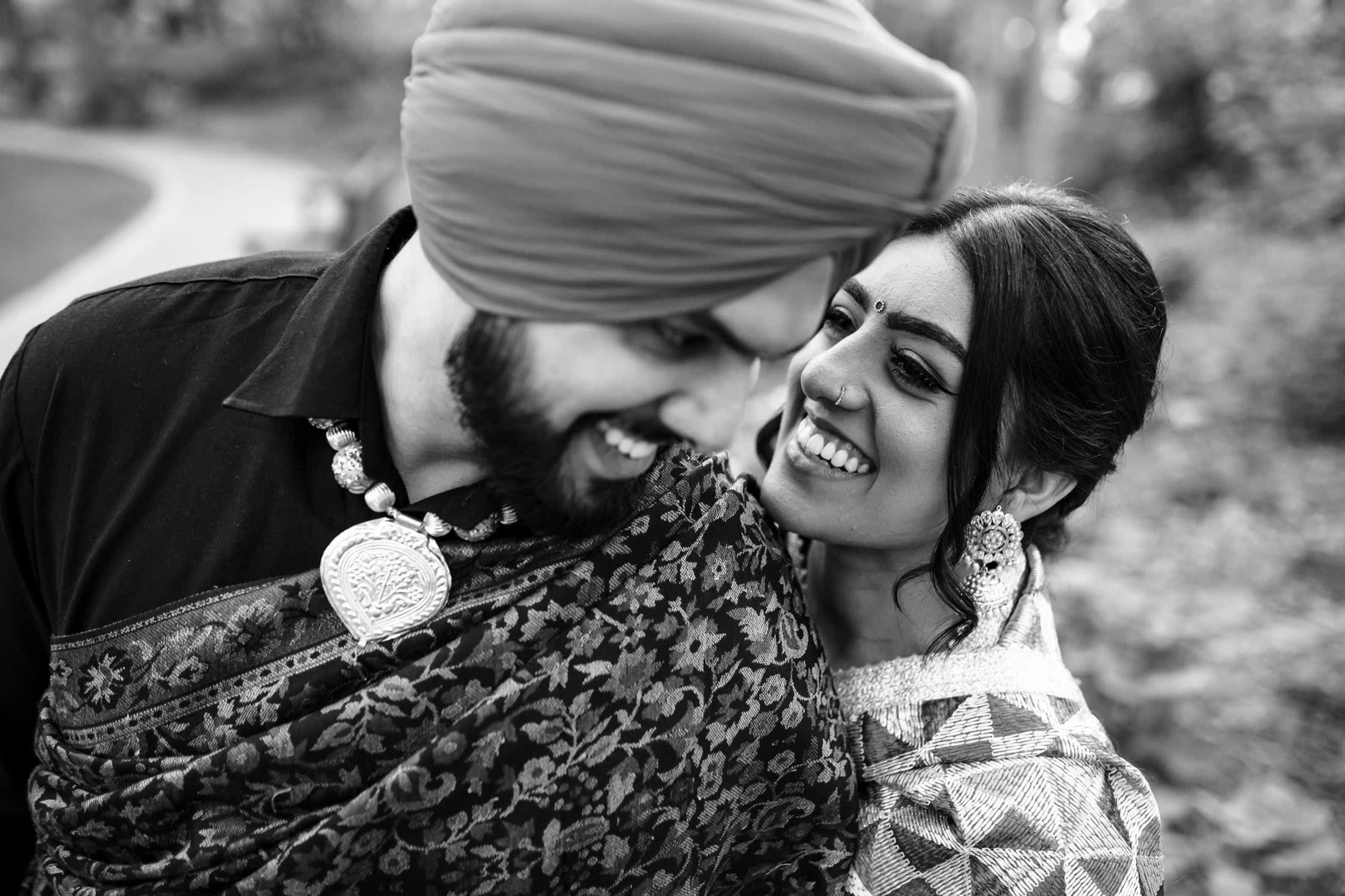 A couple smiling at each other in traditional attire, with one wearing a turban and decorative necklace.