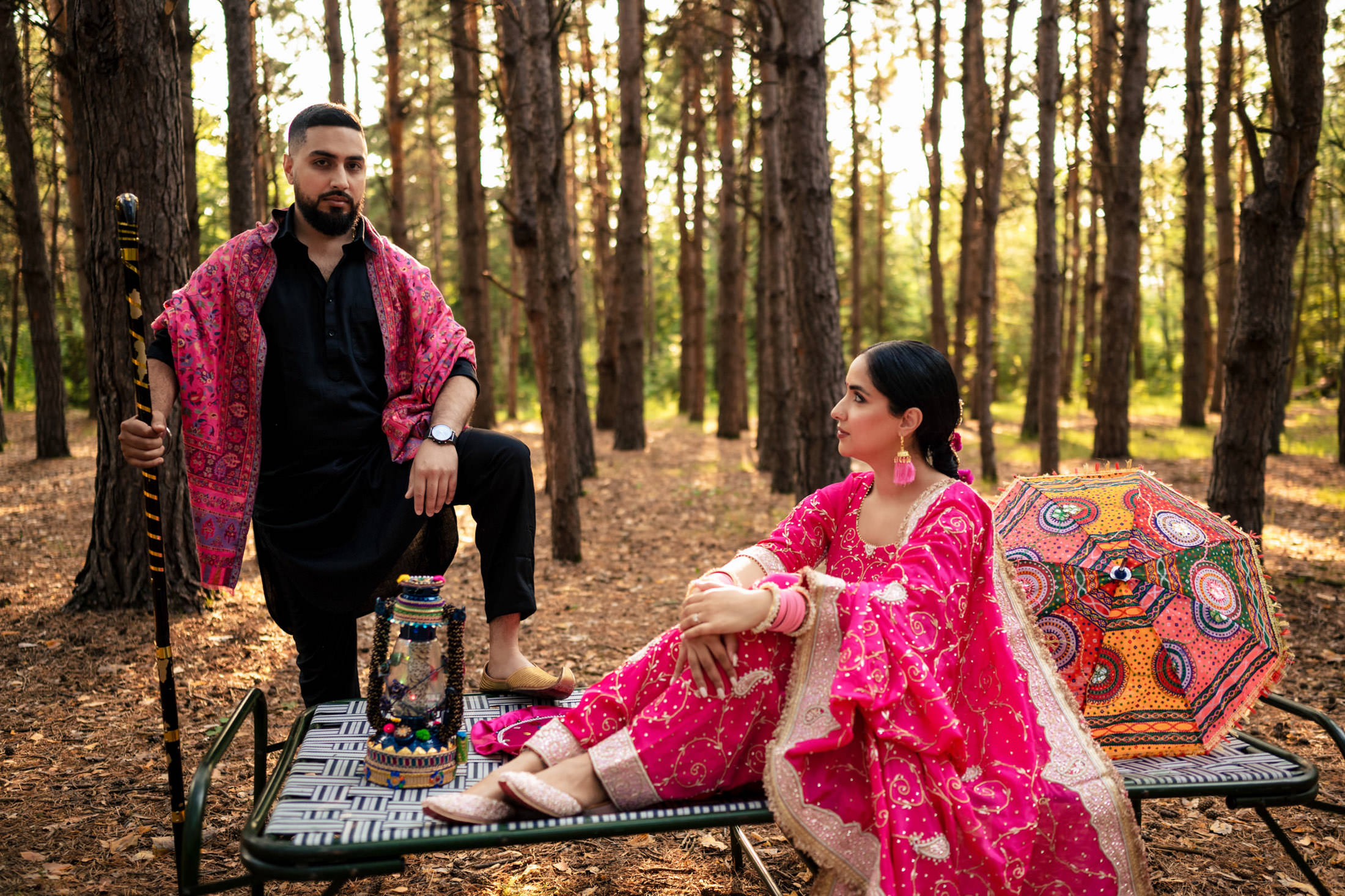 Two people in vibrant attire sitting on a bench in a sunlit forest.