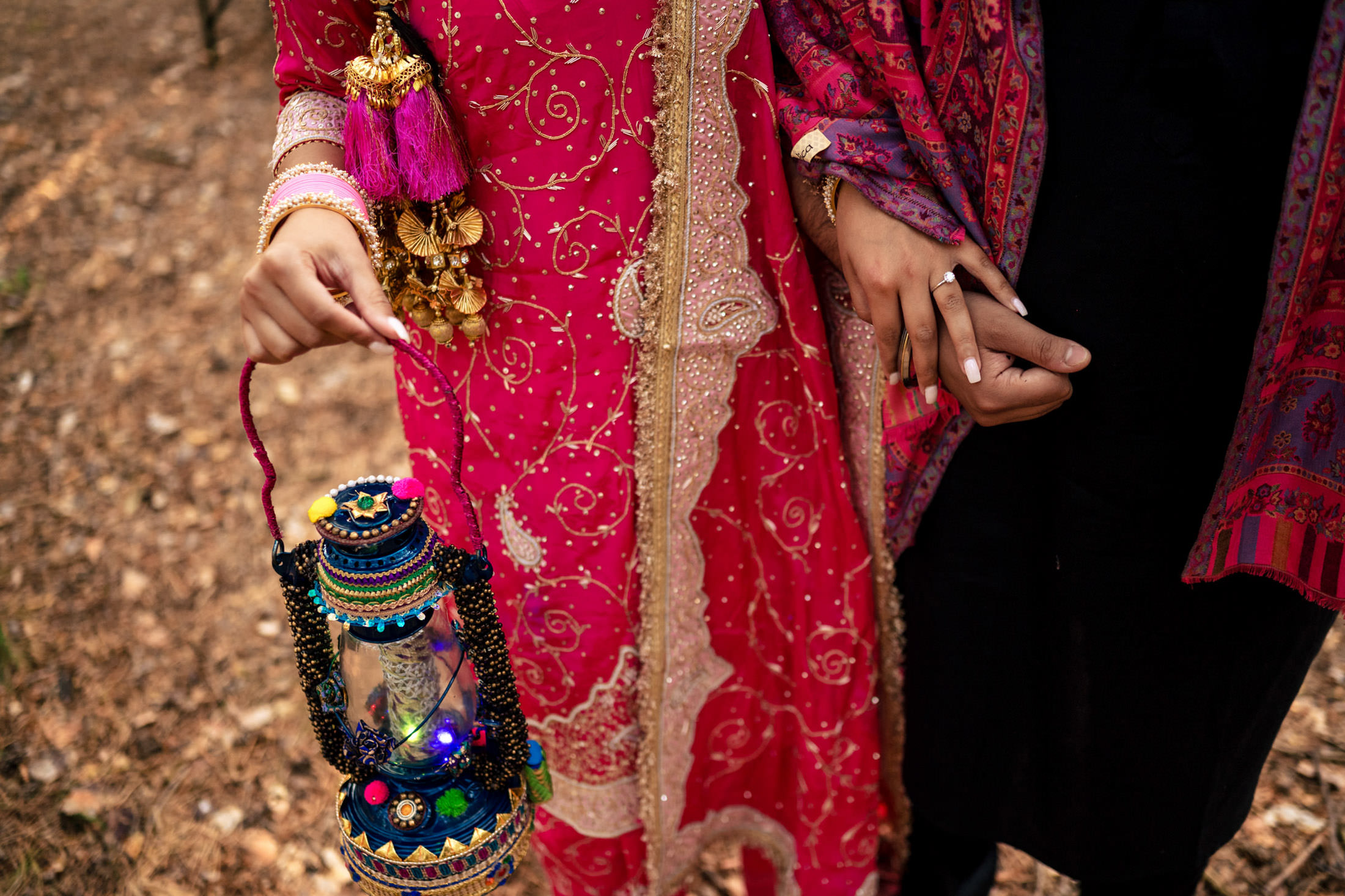 Couple holding hands, one holding a colorful lantern, dressed in ornate traditional attire.