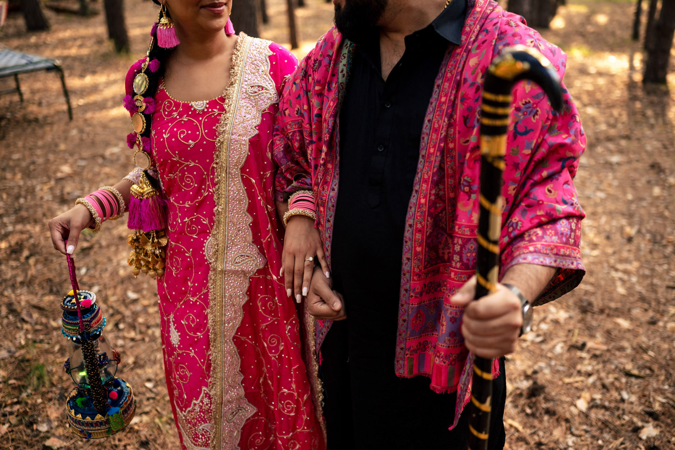 Couple in traditional attire, holding hands in a wooded area.