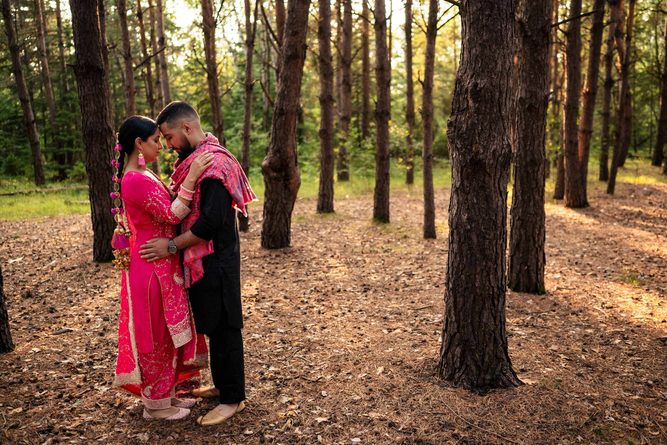 Couple in traditional attire embraces in a sunlit forest.