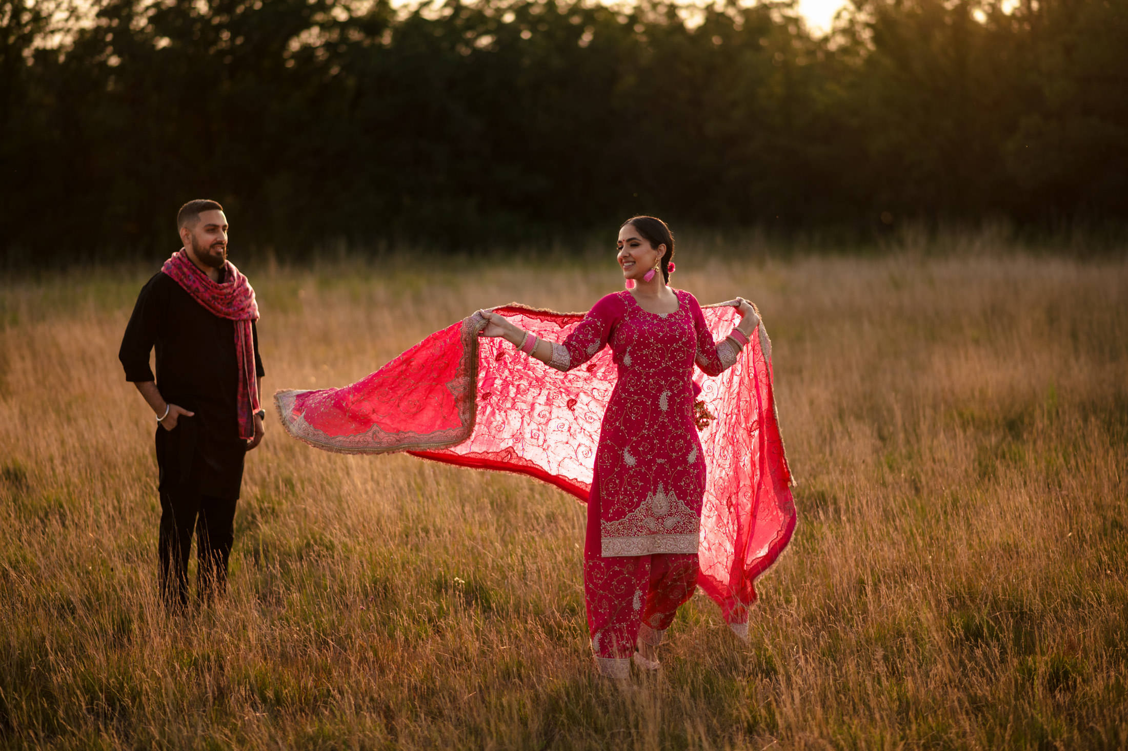 Two people in a field, one in a vibrant pink outfit with a flowing shawl.