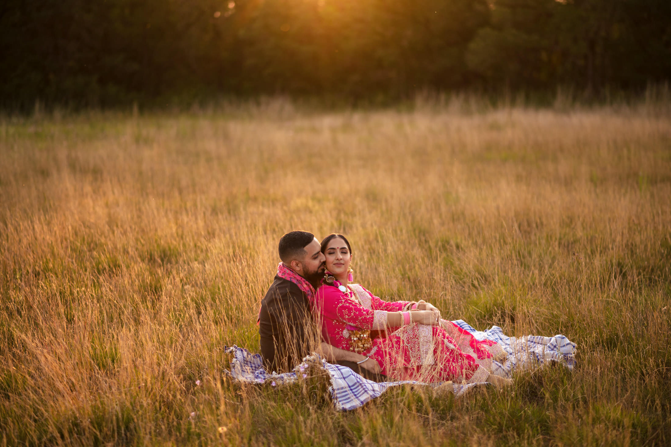 Couple sitting on a blanket in a grassy field during sunset.