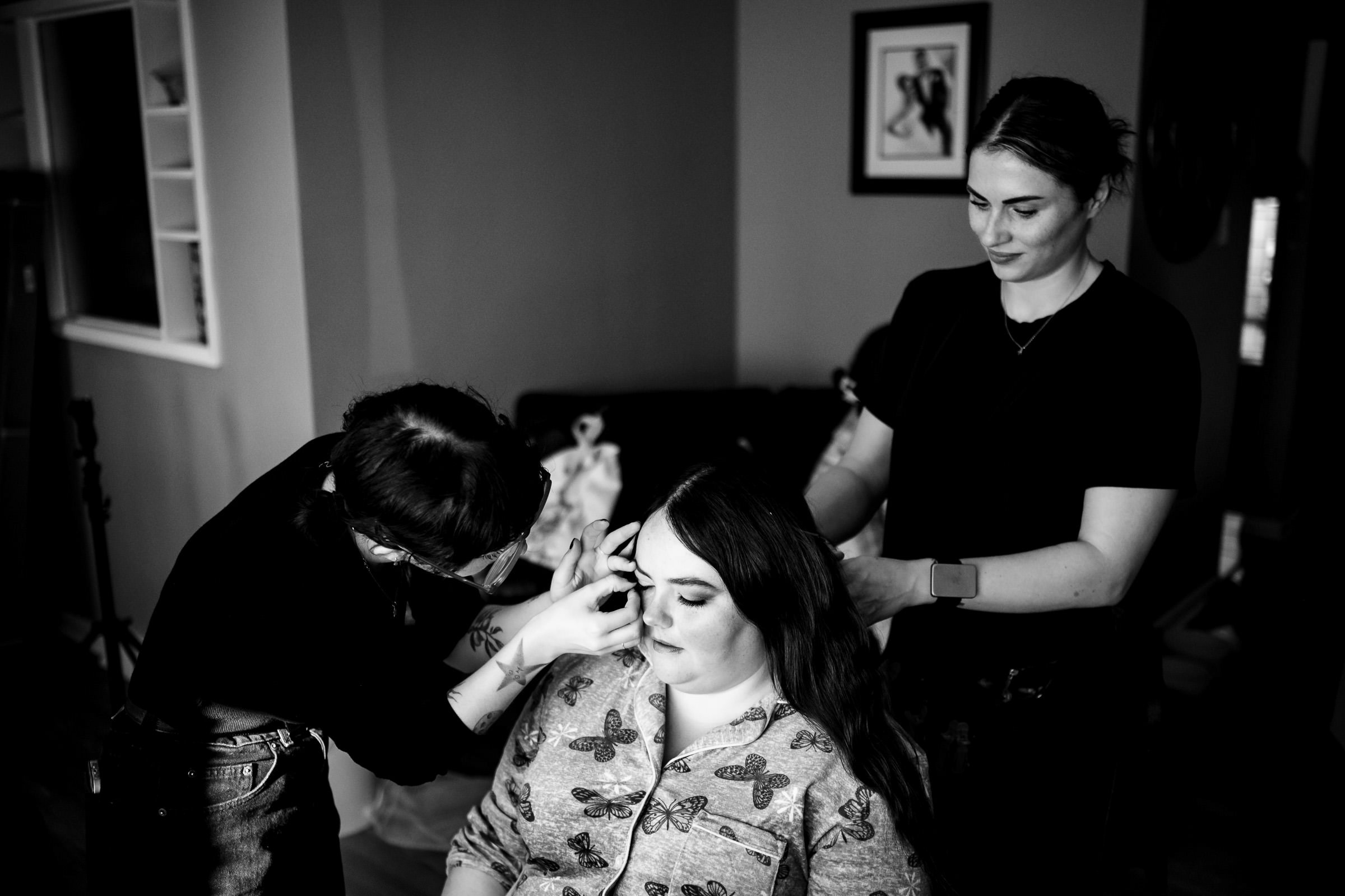 Two people style a woman's makeup and hair in a room.