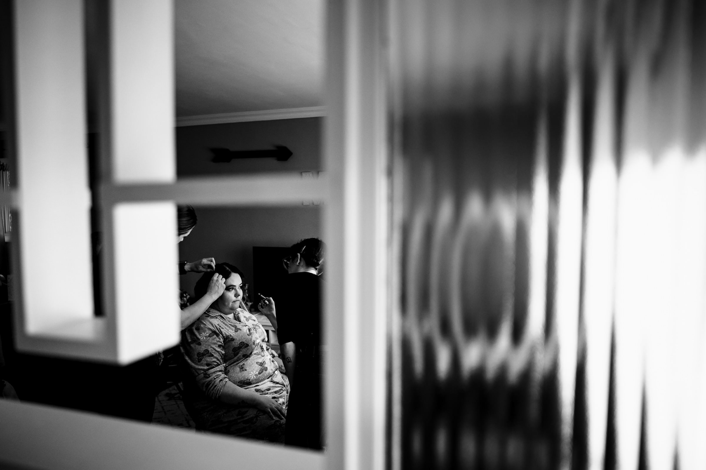 Person getting makeup done, seated in a room, seen through a partially open door.