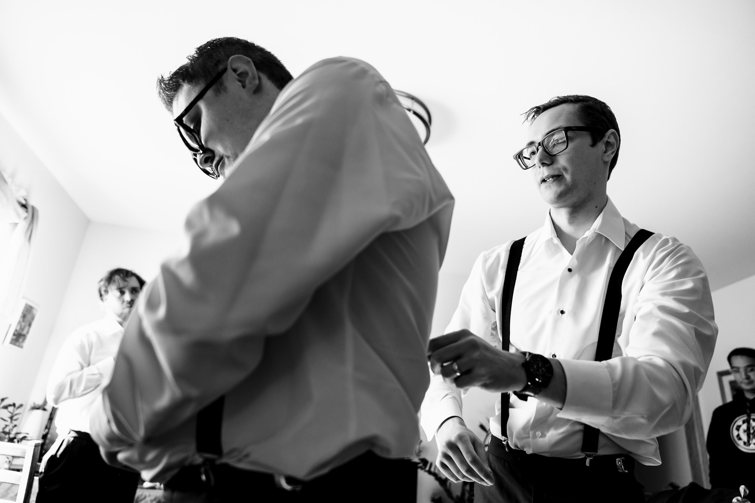 Two people in dress shirts adjusting suspenders in a room. Black and white photo.
