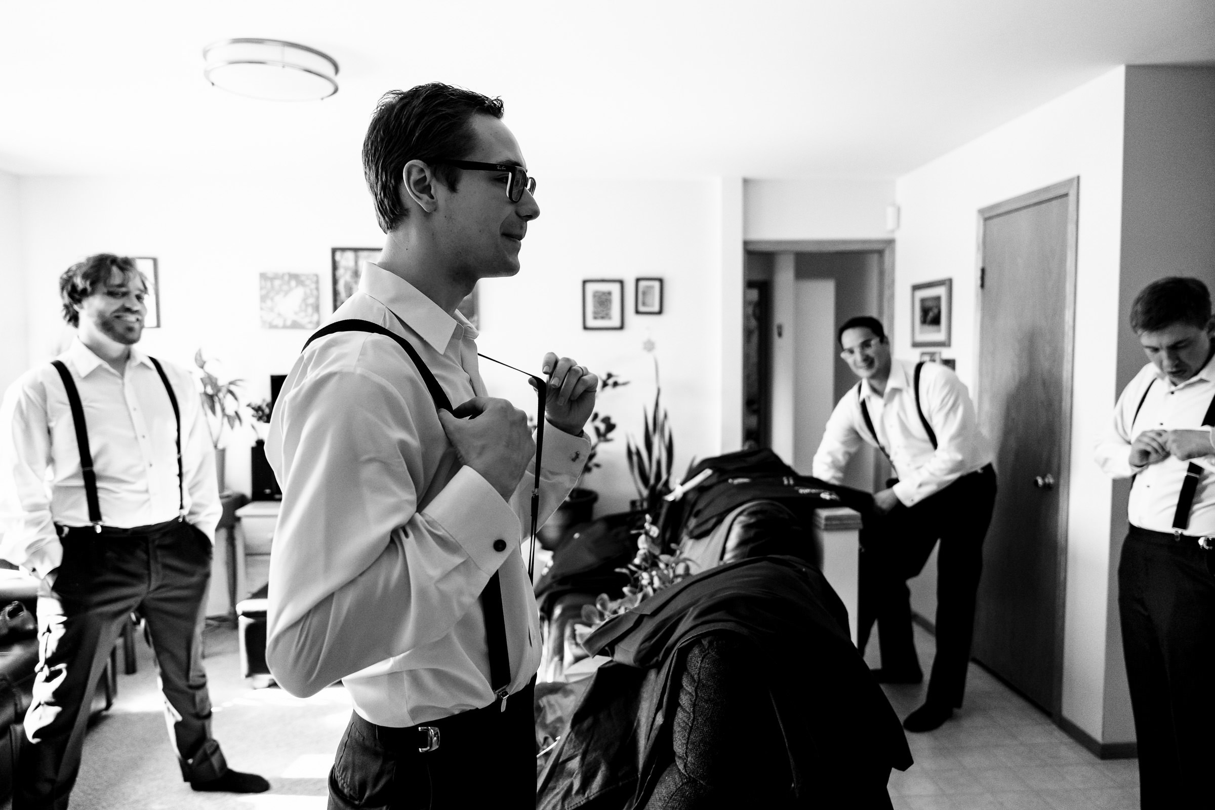 A group of four men in formal shirts and suspenders, preparing in a room.