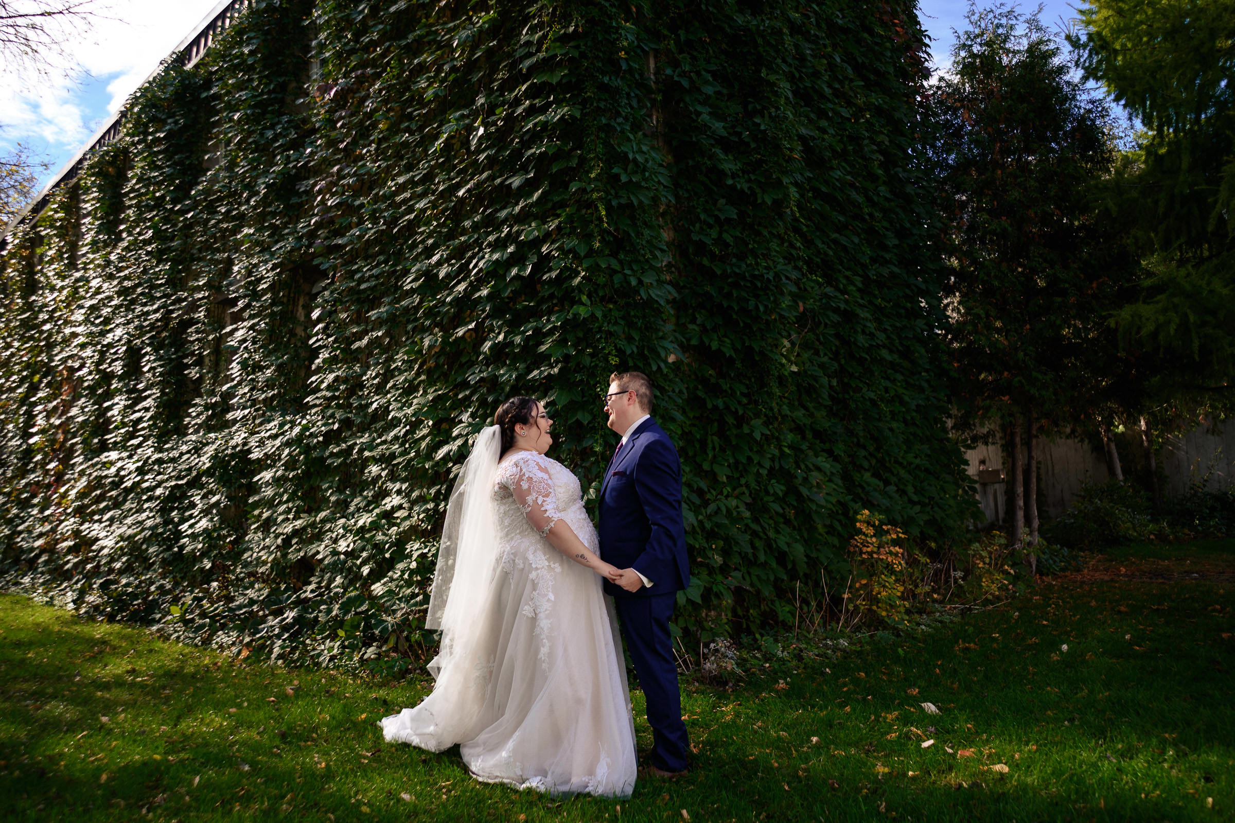 Bride and groom hold hands, standing by an ivy-covered building.