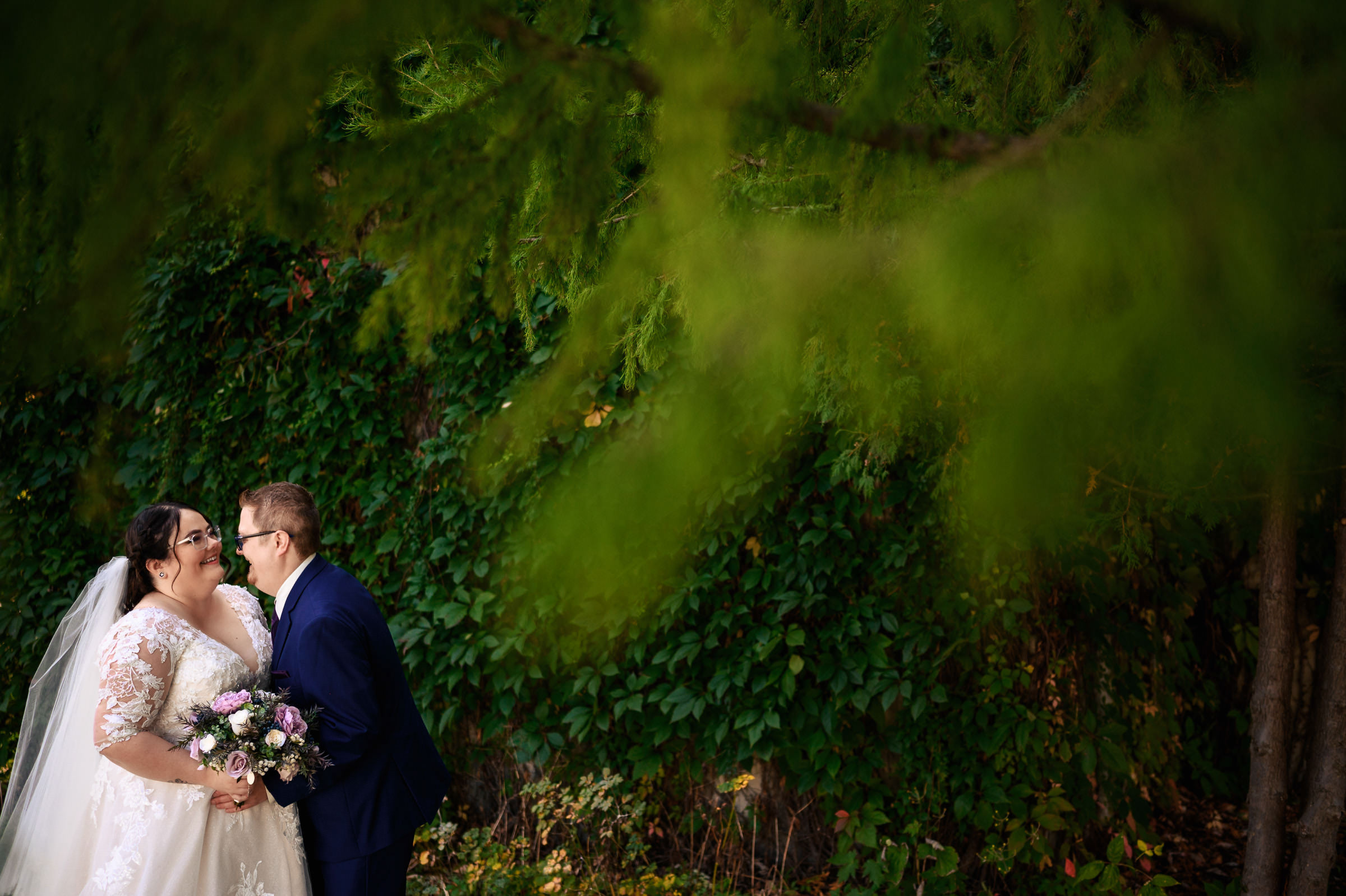 Bride and groom smiling under lush greenery.