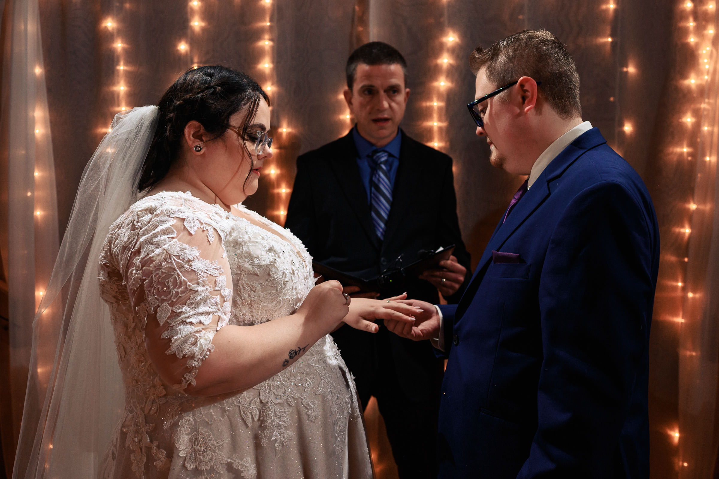 A couple exchanges rings during their wedding ceremony with an officiant present.