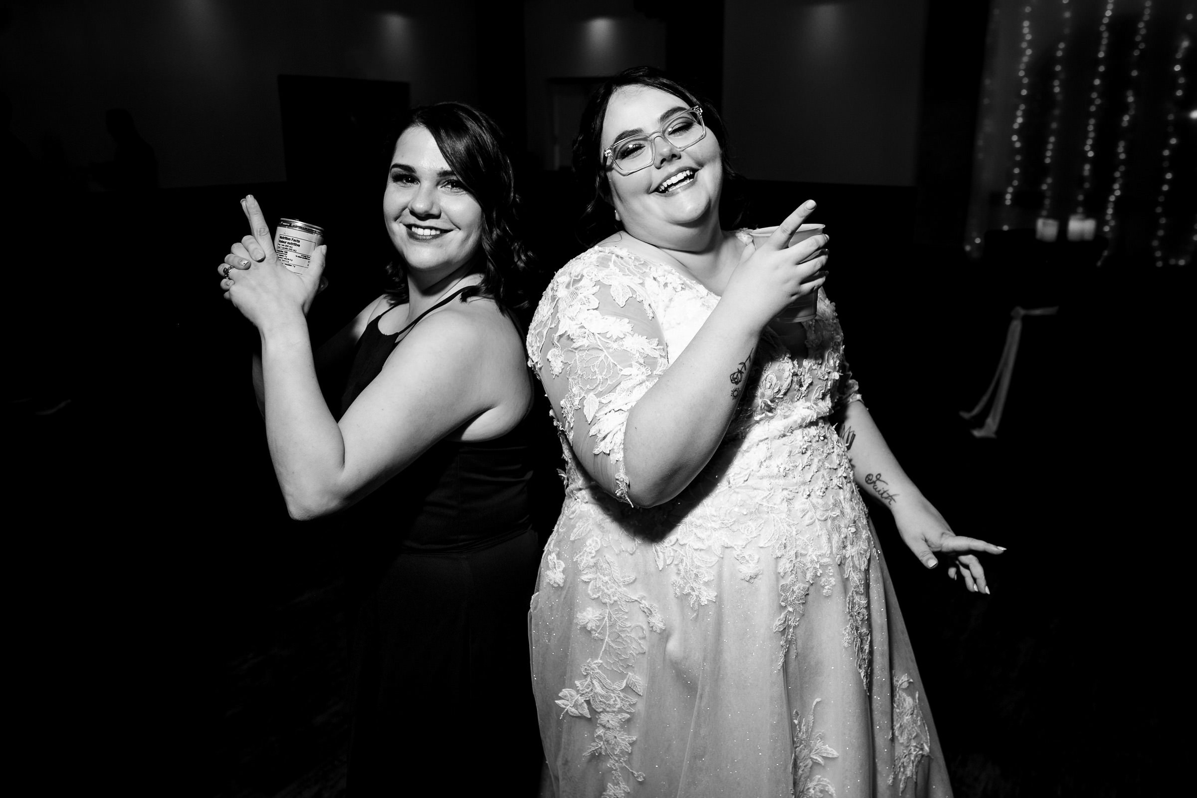 Two women back to back, smiling and holding drinks, in formal attire.