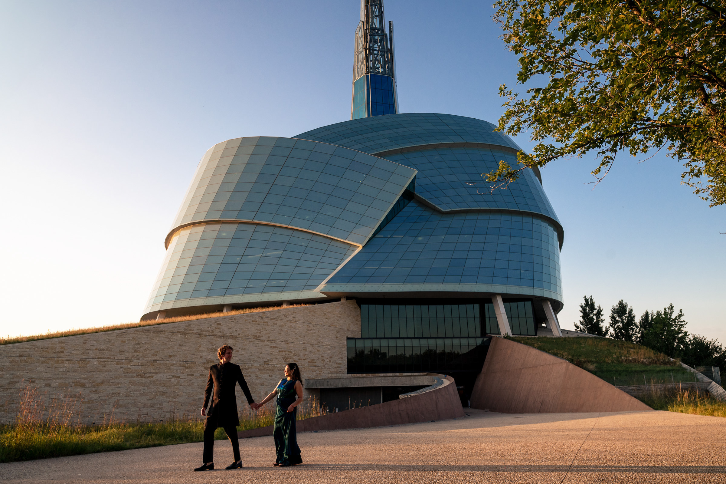 A couple holds hands near a glass-paneled tower, capturing a Winnipeg wedding moment.
