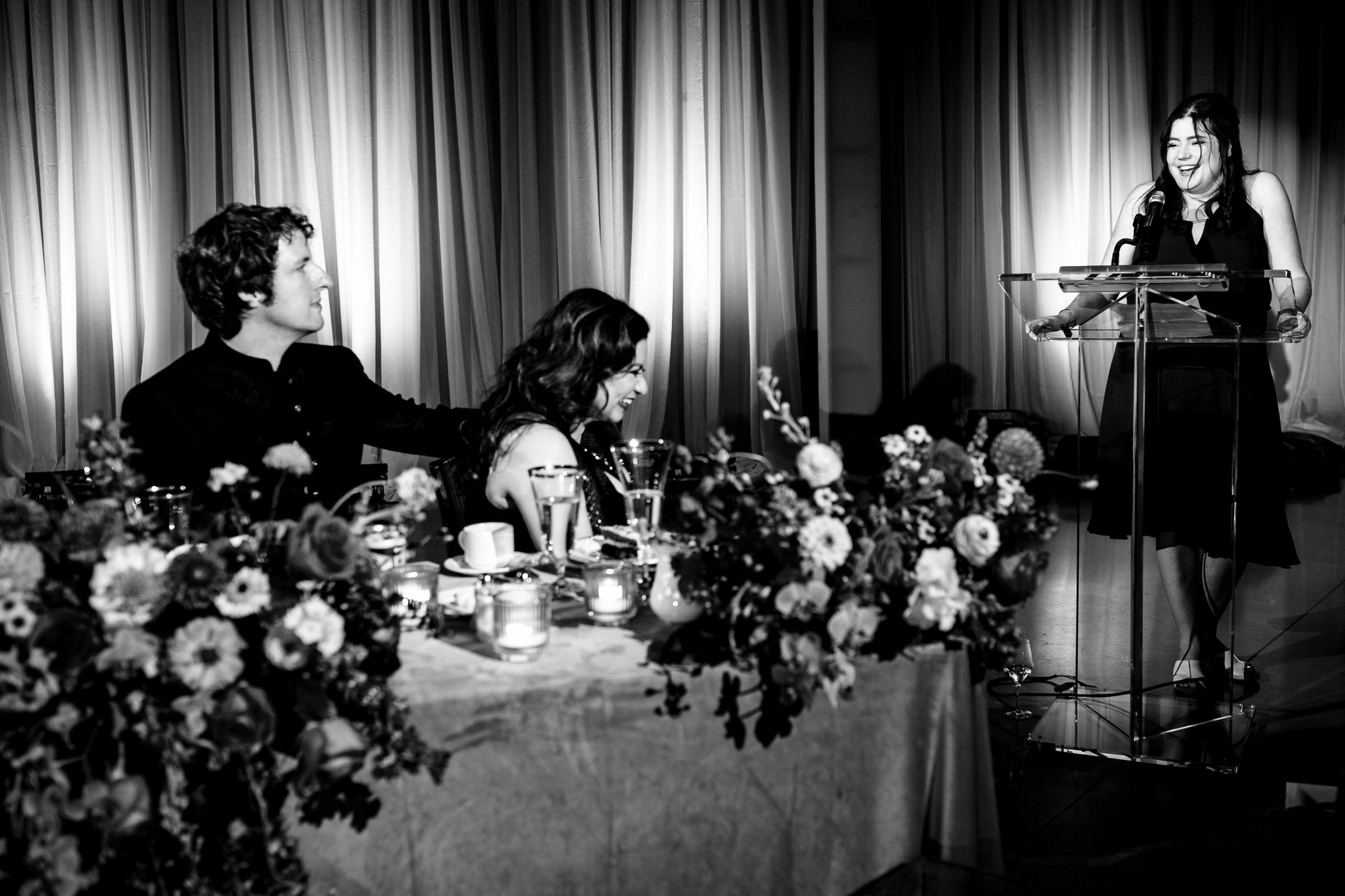 At a Winnipeg wedding, a woman speaks at a podium; guests at the table listen and laugh.