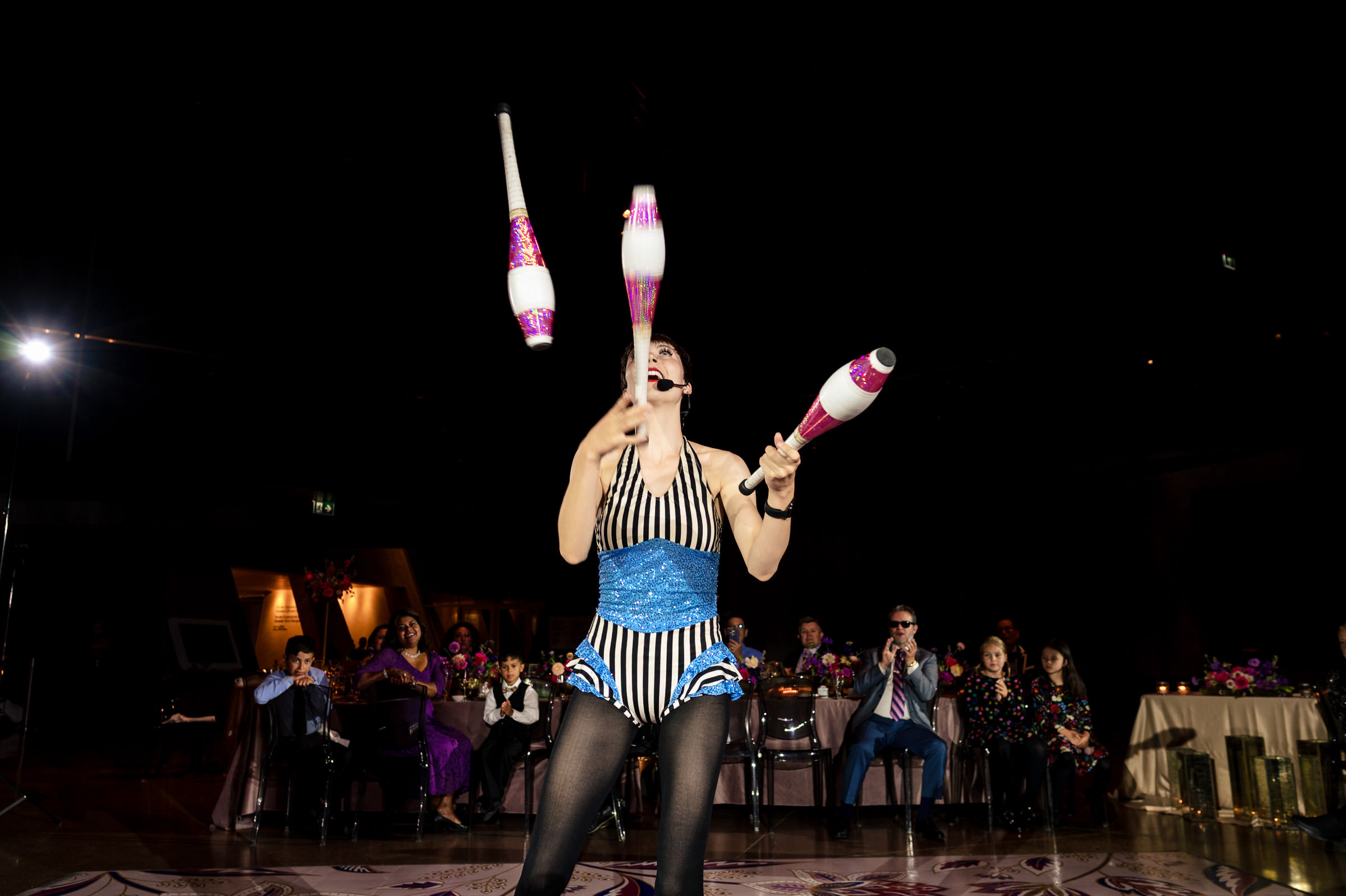 Juggler in blue dazzles with clubs on a dimly lit Winnipeg wedding stage.
