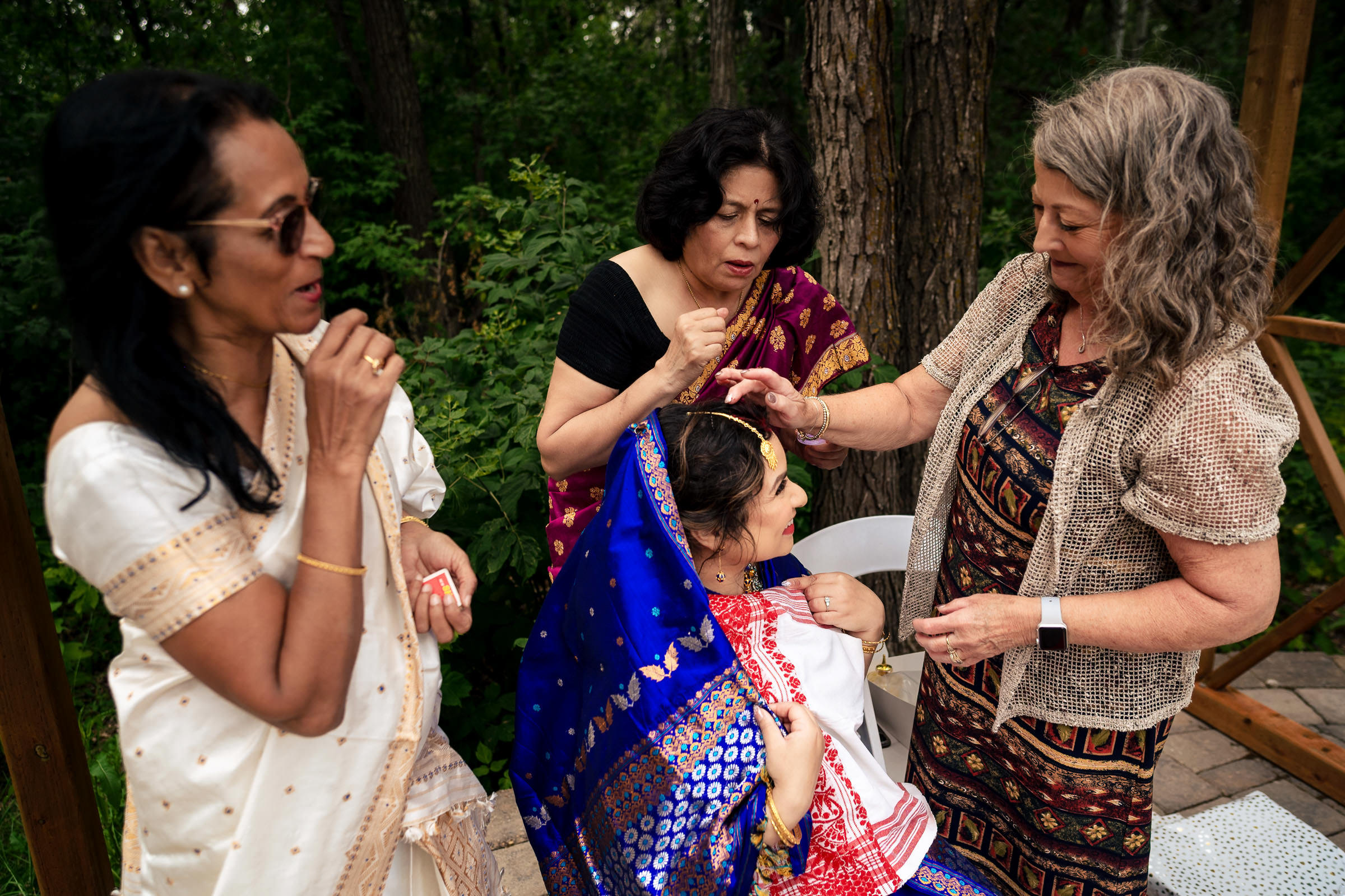 Three women assist the bride in a vibrant blue and red saree at a Winnipeg wedding.