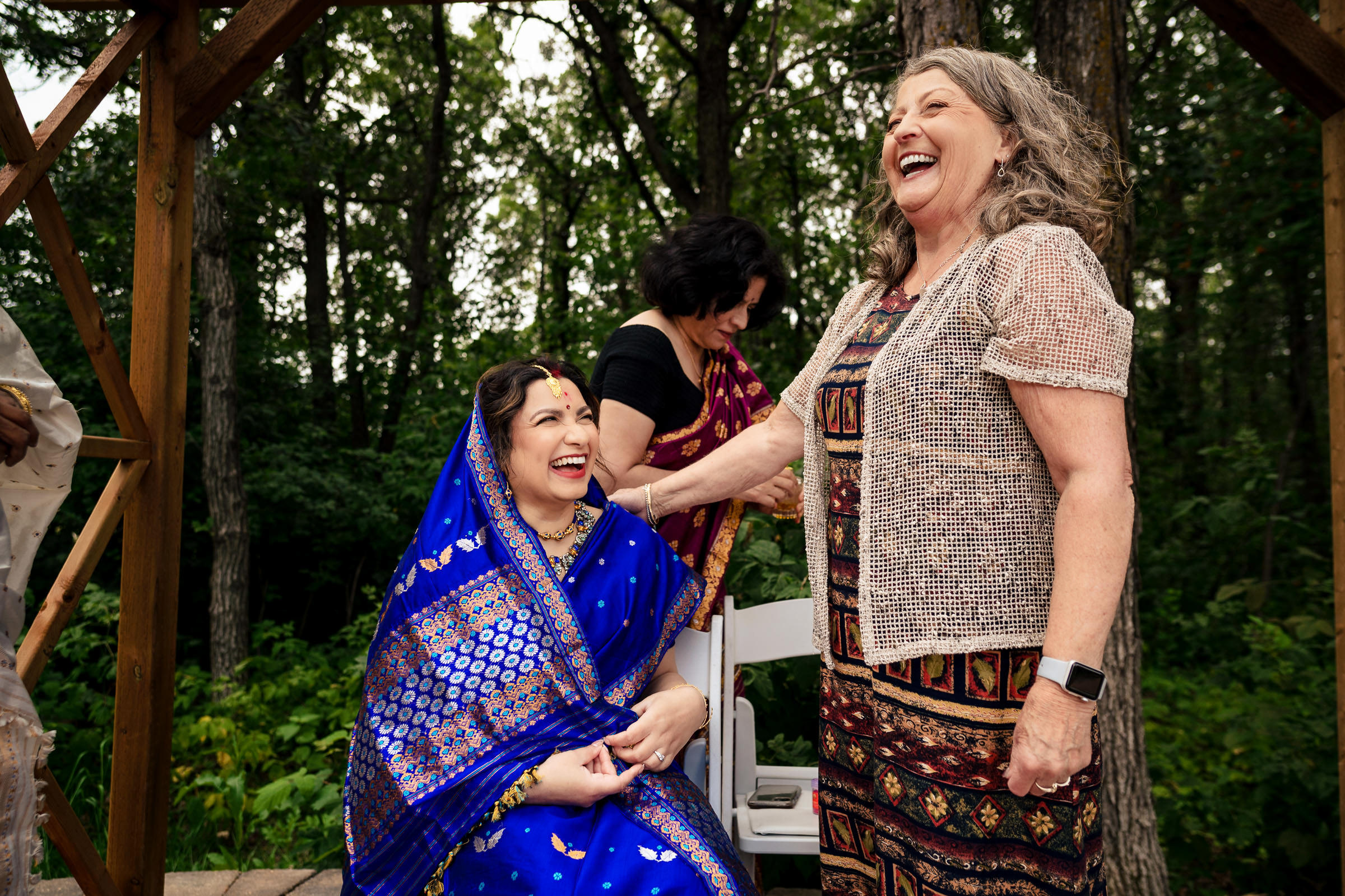 Two women laugh together at a Winnipeg wedding; one wears a vibrant blue sari.